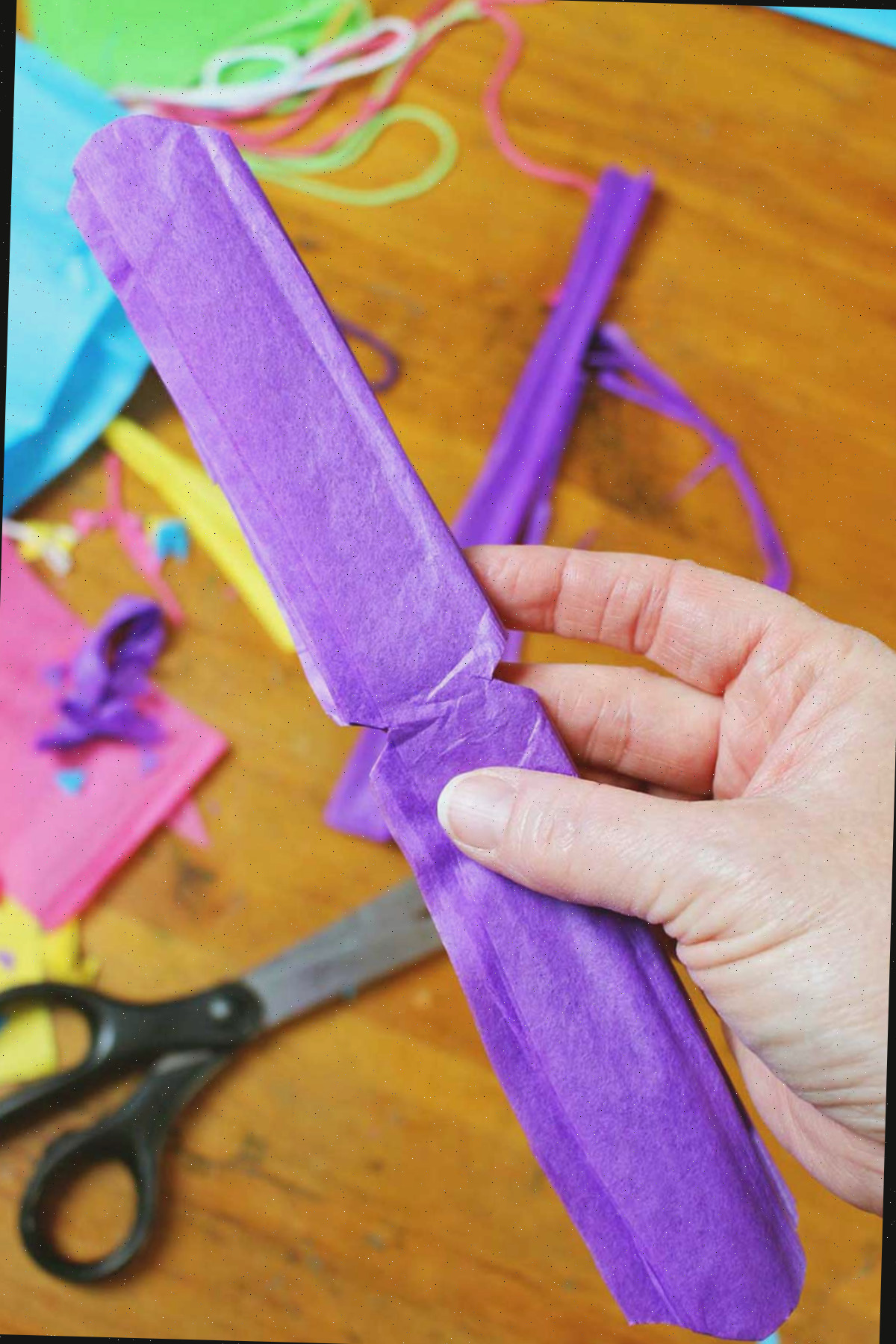Mão segurando papel crepom roxo dobrado e aparado.