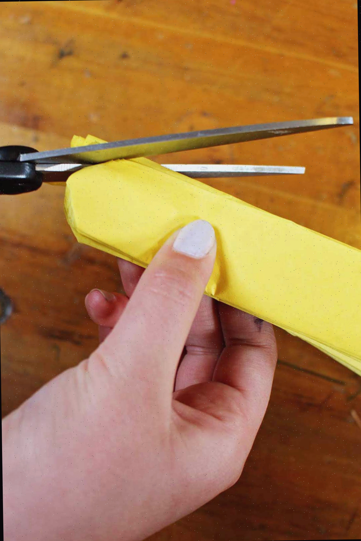 Uma mão cortando as extremidades do papel crepom amarelo dobrado para criar uma borda arredondada com tesoura.
