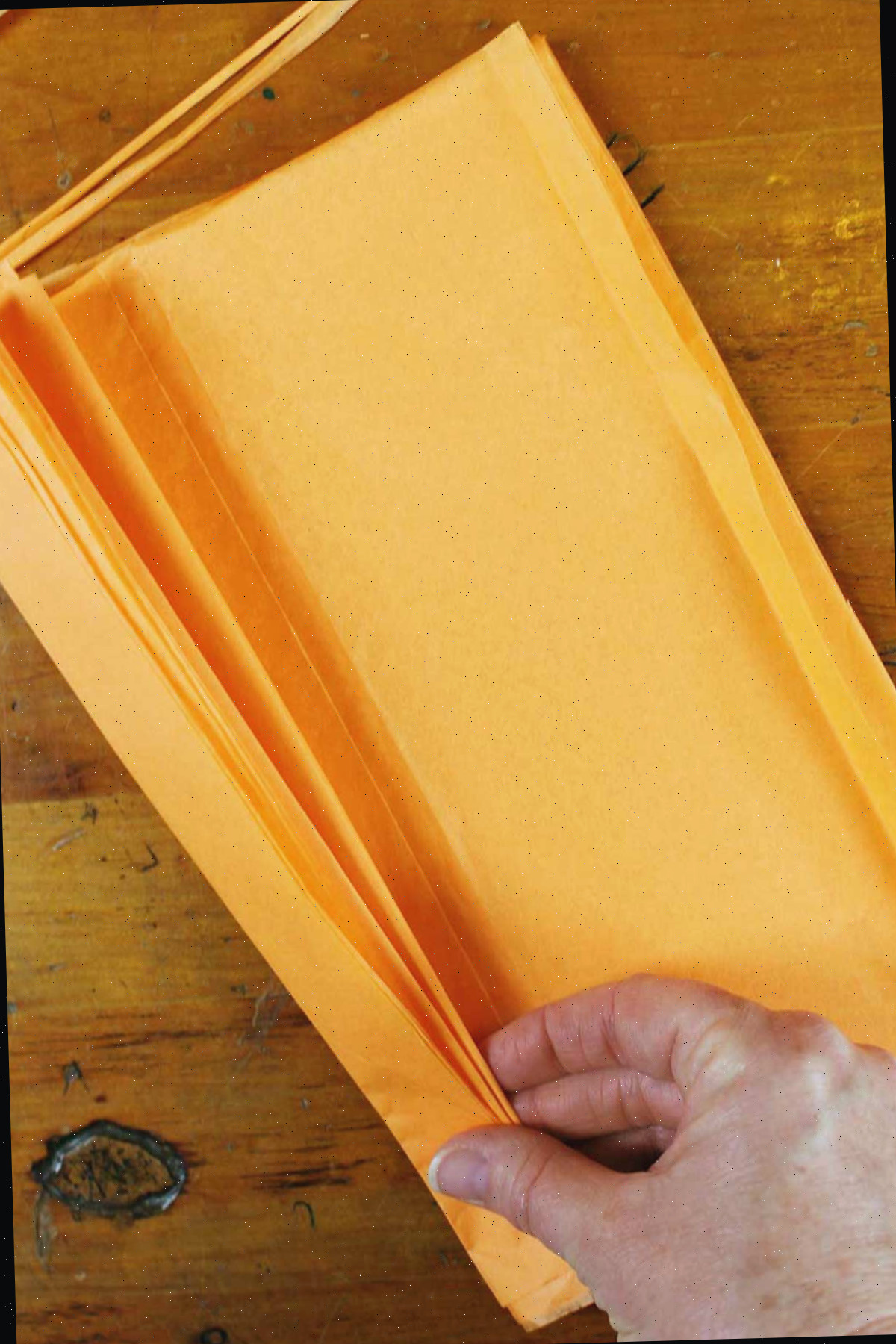 Mão dobrando uma pilha de papel de seda laranja.