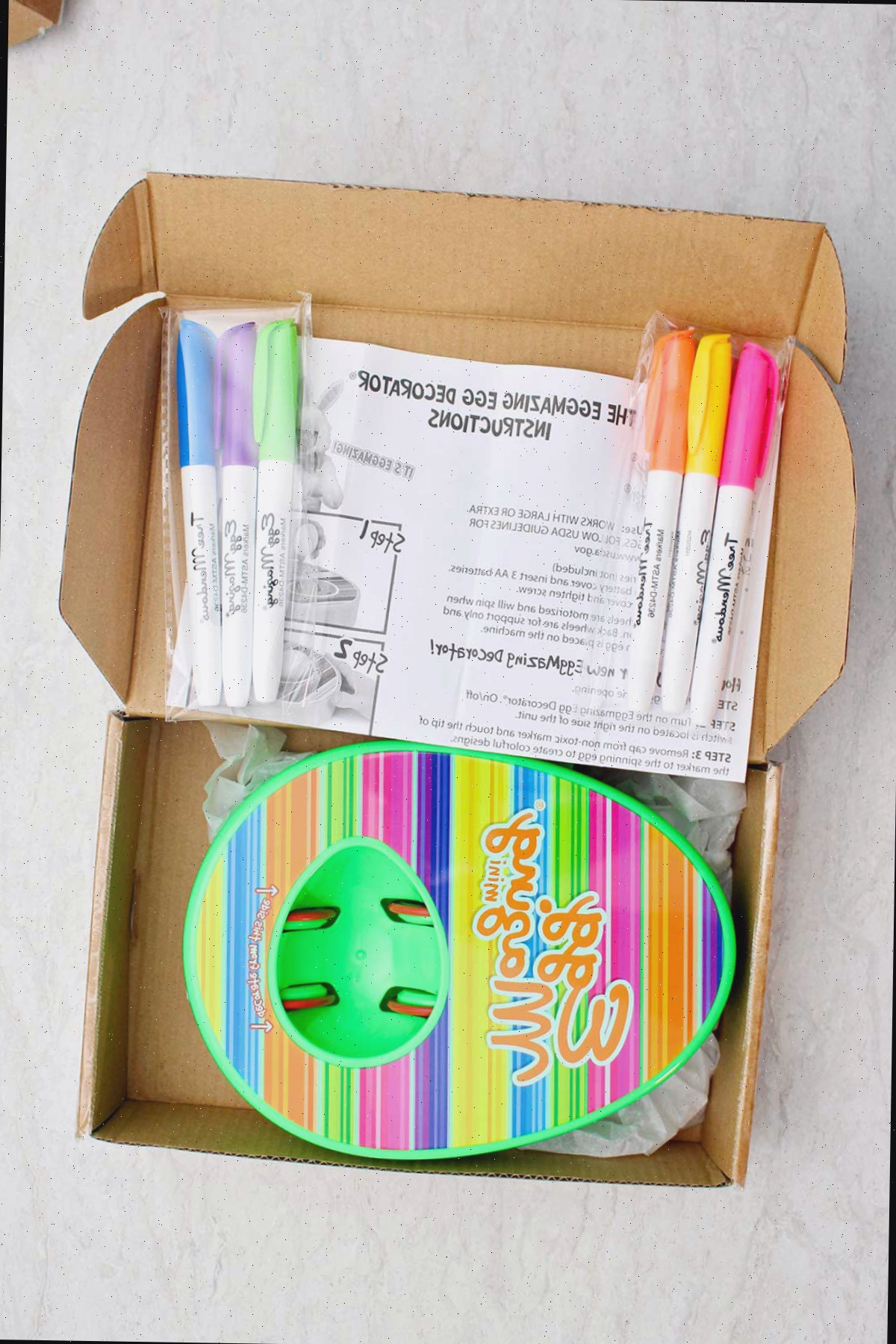 Uma caixa cheia de um kit EggMazing, marcadores e instruções.