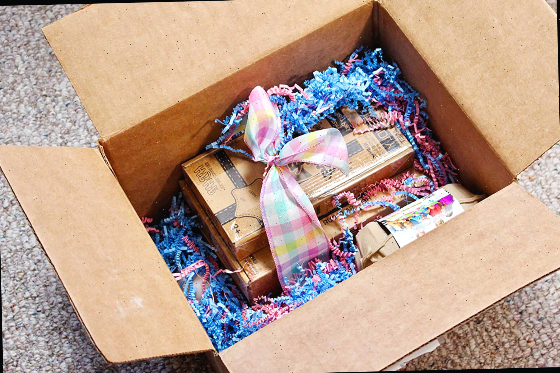 Uma caixa repleta de um presente de kits EggMazing, ovos de madeira e grama de Páscoa.