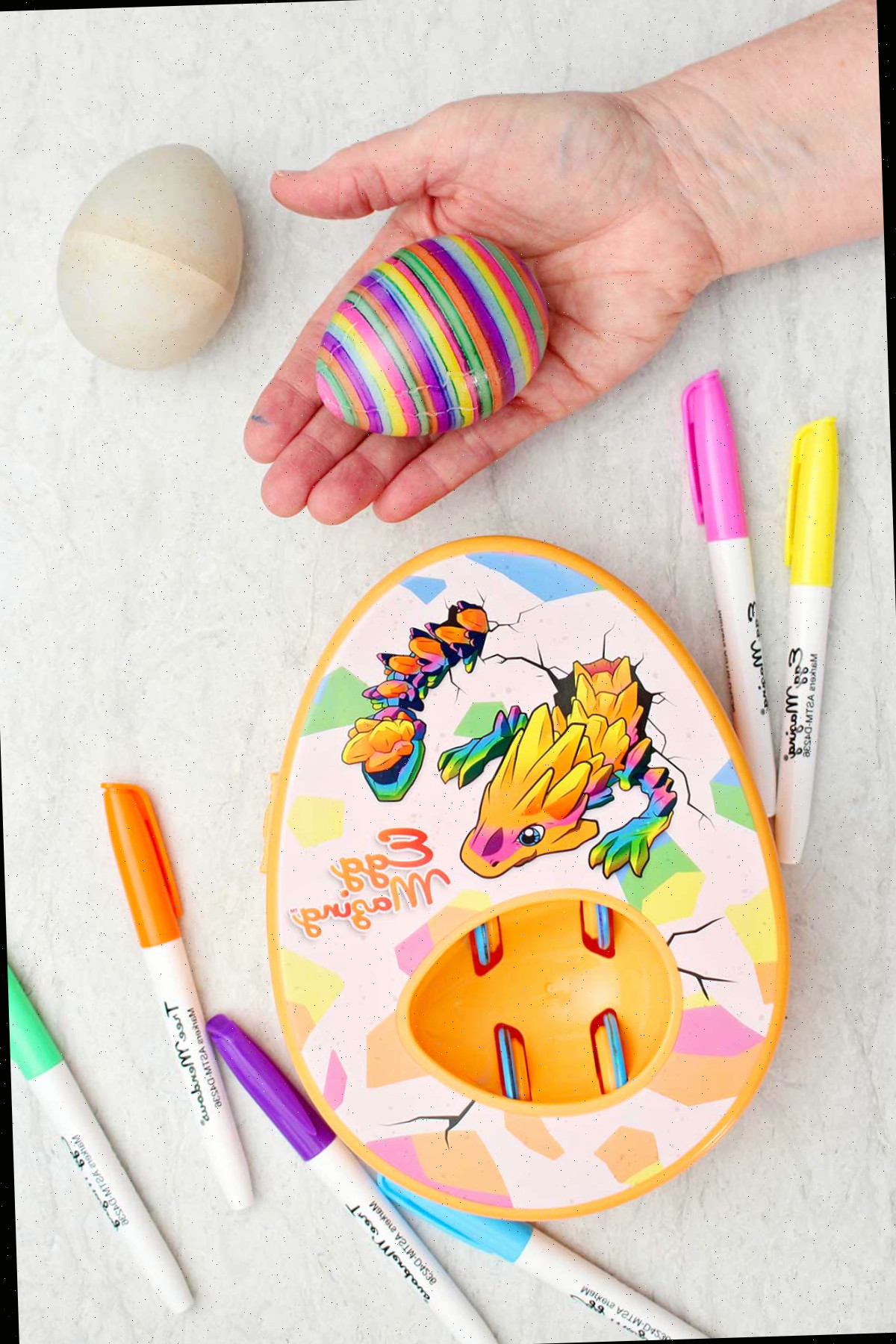 Uma pessoa segurando um ovo colorido listrado com o kit Dragão EggMazing ao lado.