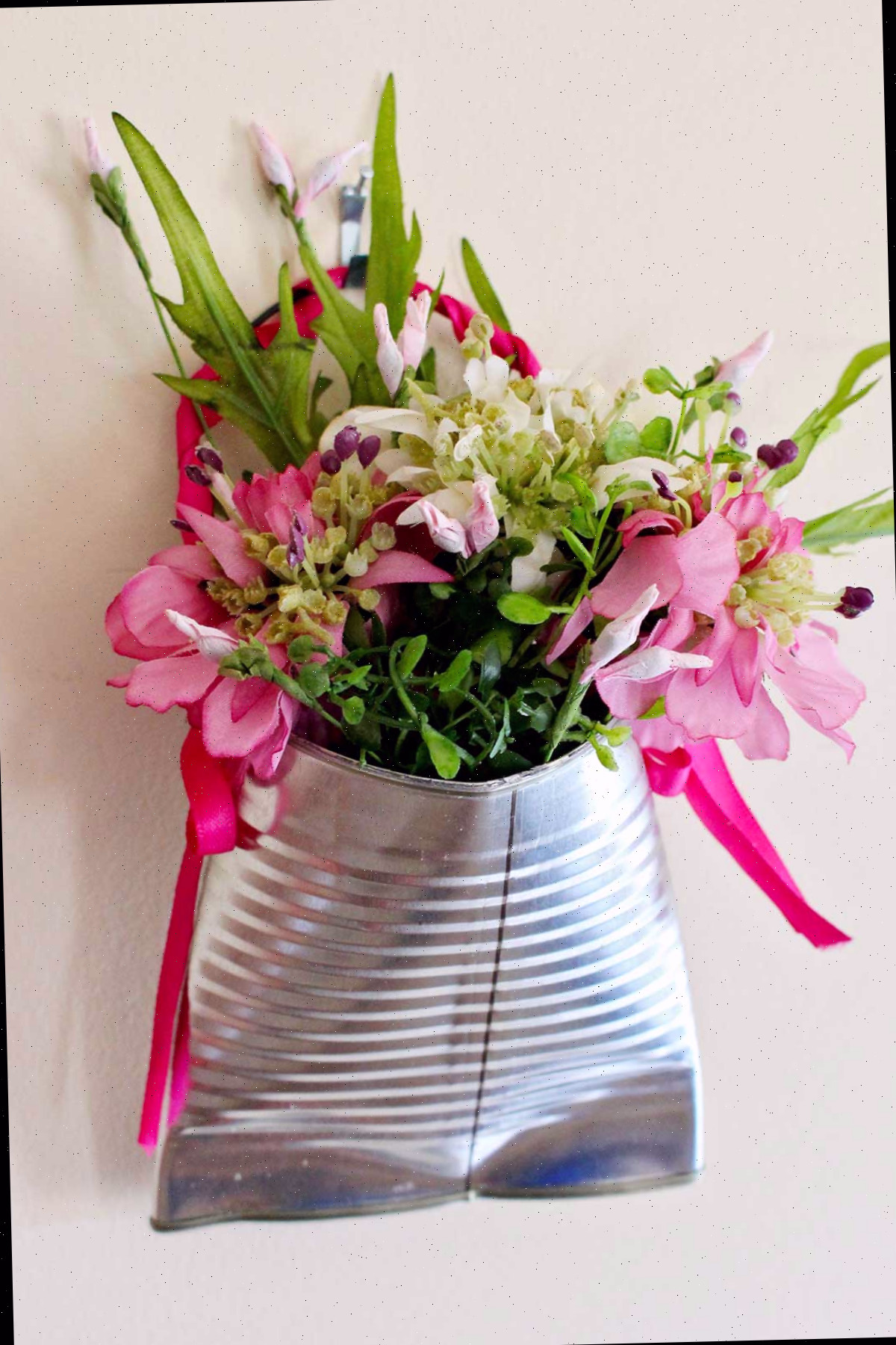 Um vaso de flores de lata reutilizada recheado com flores rosas e folhagens.