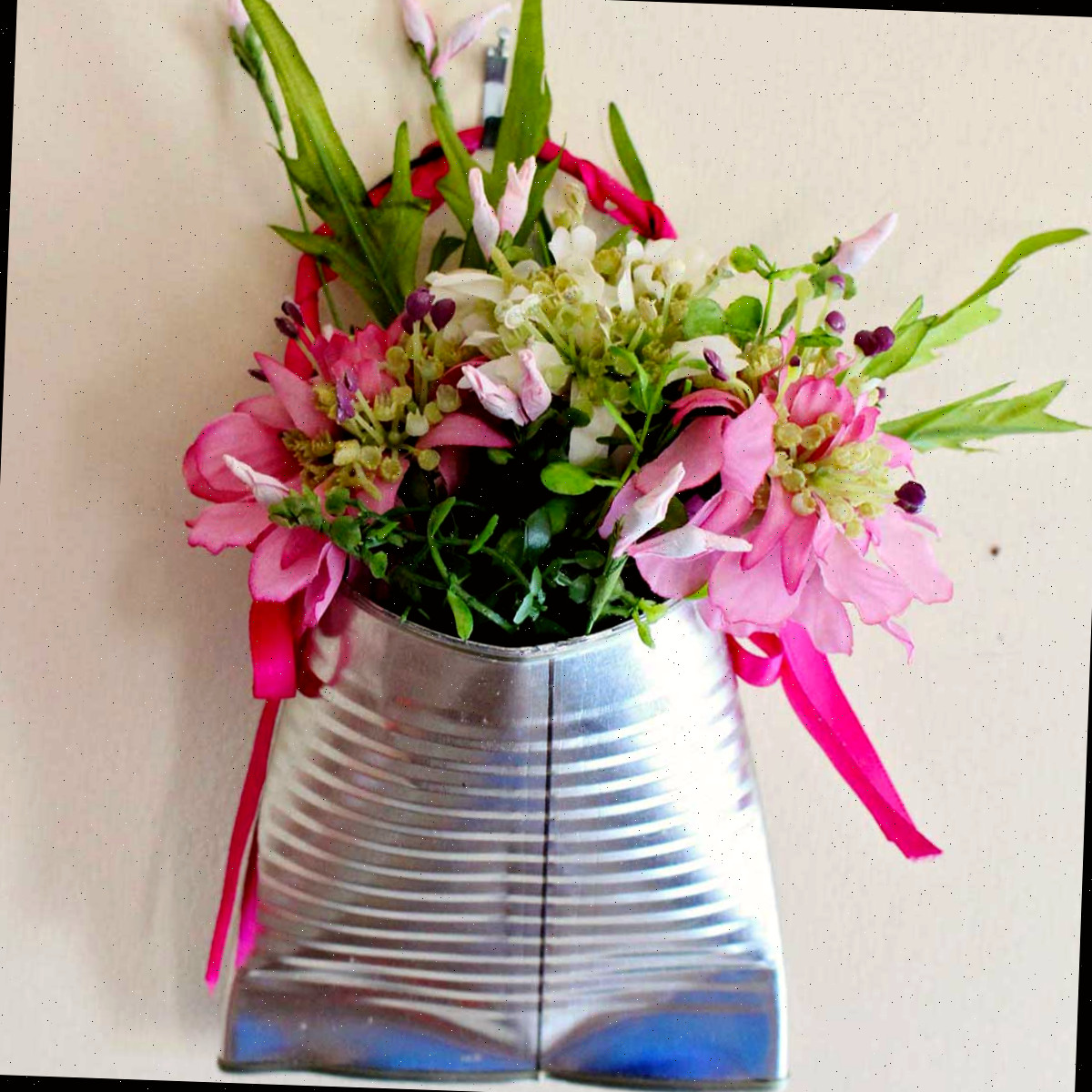 Um vaso de flores de lata reciclada completo, cheio de flores rosas e folhagens.