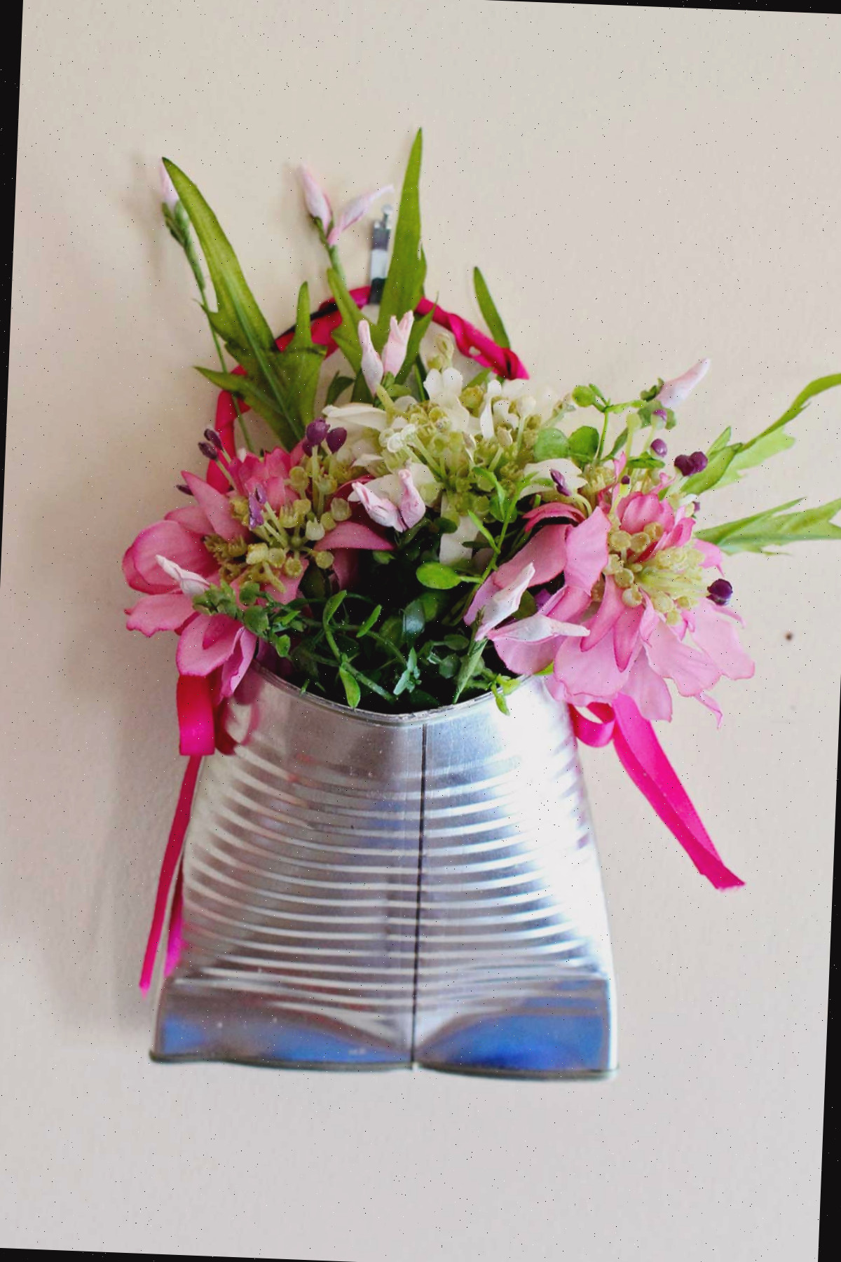 Um vaso de lata reciclado completo, cheio de flores rosas e folhagens.