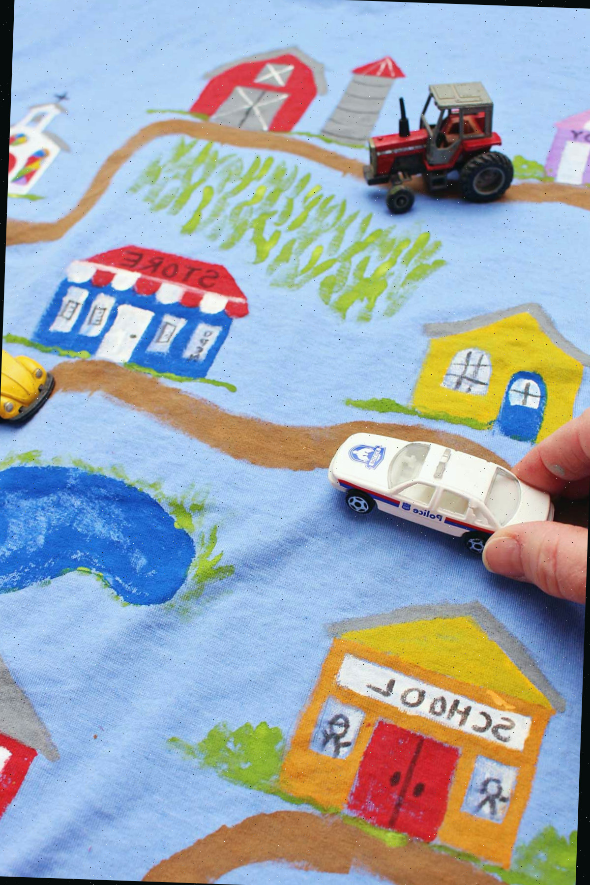 Uma pessoa dirigindo um carro de polícia em uma camiseta do Dia dos Pais completa, exibindo uma estrada de terra que leva a vários edifícios da cidade.