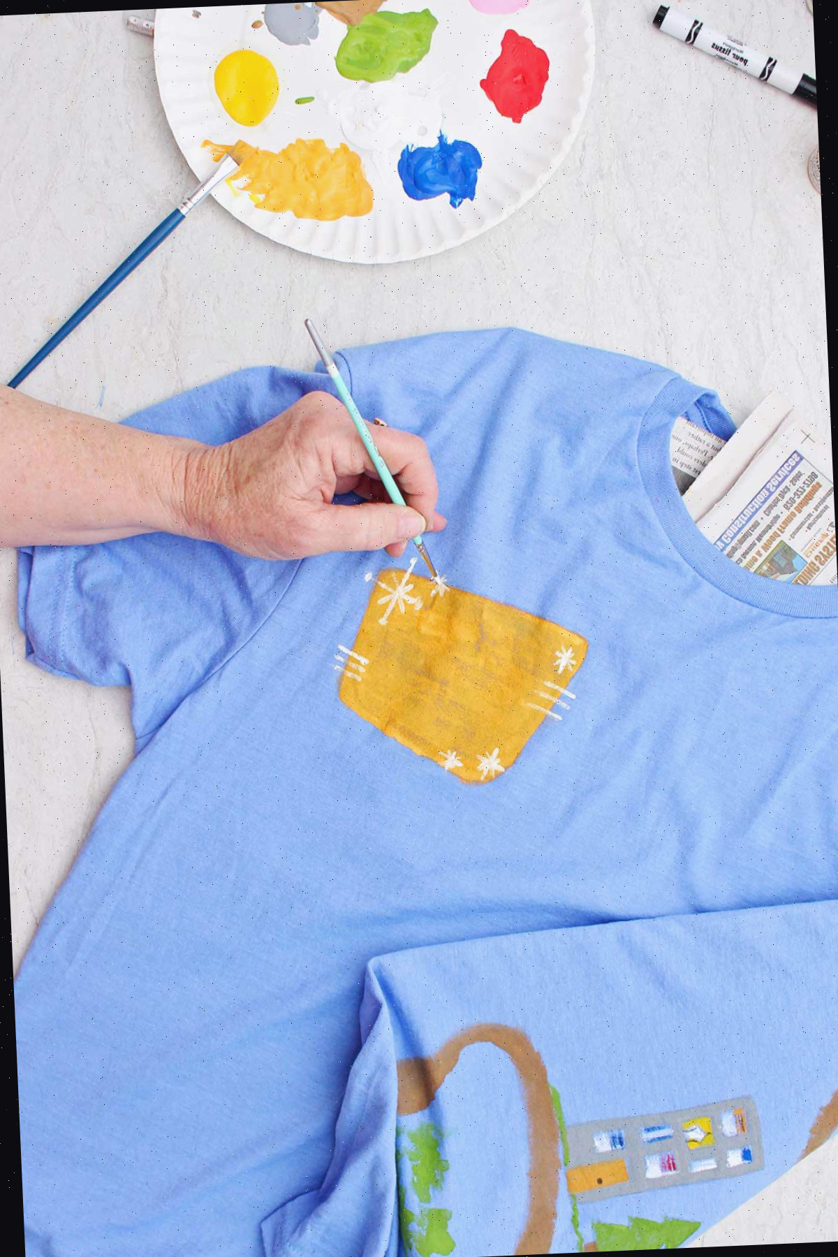Uma pessoa pintando detalhes brancos ao redor de uma placa amarela na parte da frente da camiseta para o Dia dos Pais.