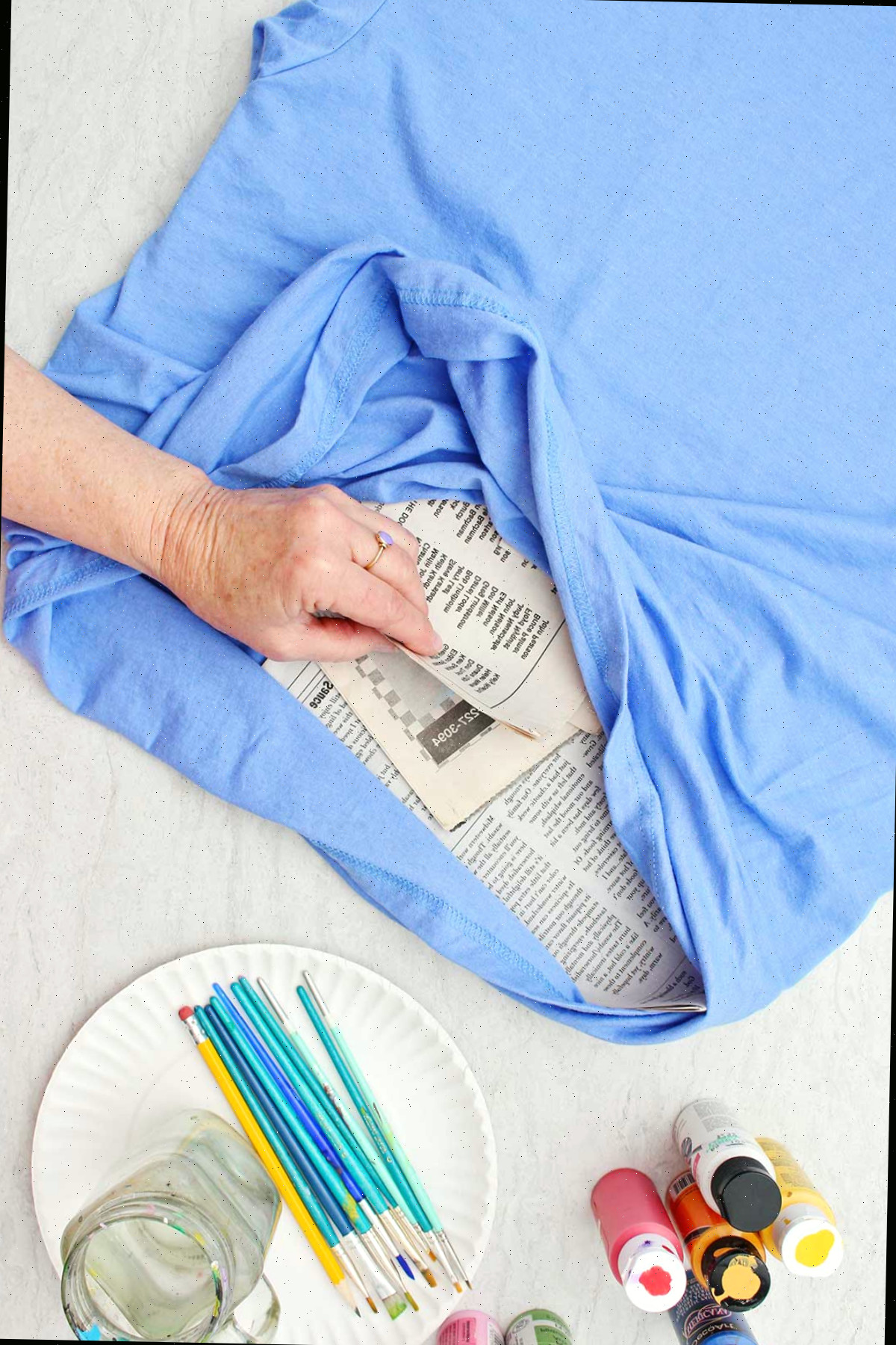 Uma pessoa colocando jornal entre os dois lados de uma camiseta azul para que a tinta não passe.