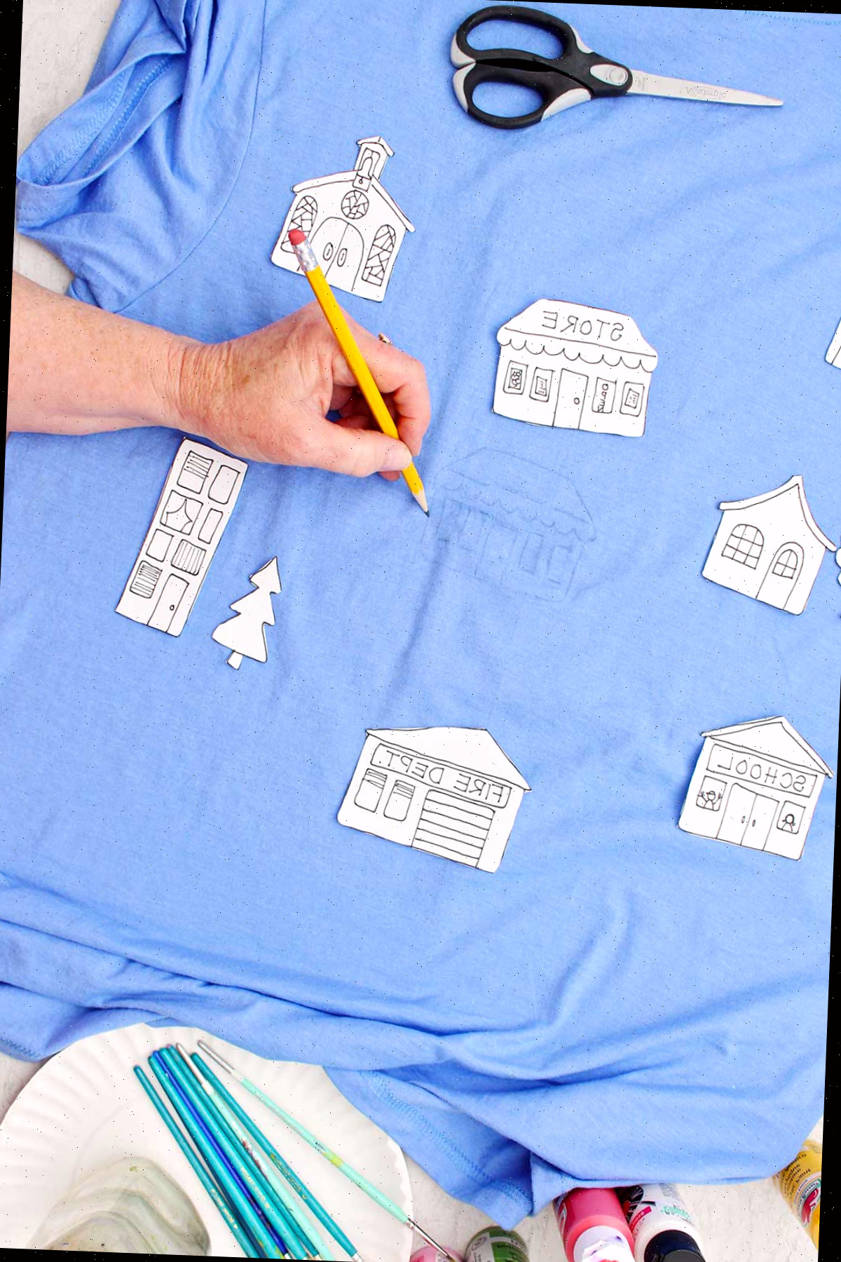 Uma pessoa desenhando detalhes em uma loja em uma camiseta azul com outros moldes de edifícios repousando sobre a camiseta.
