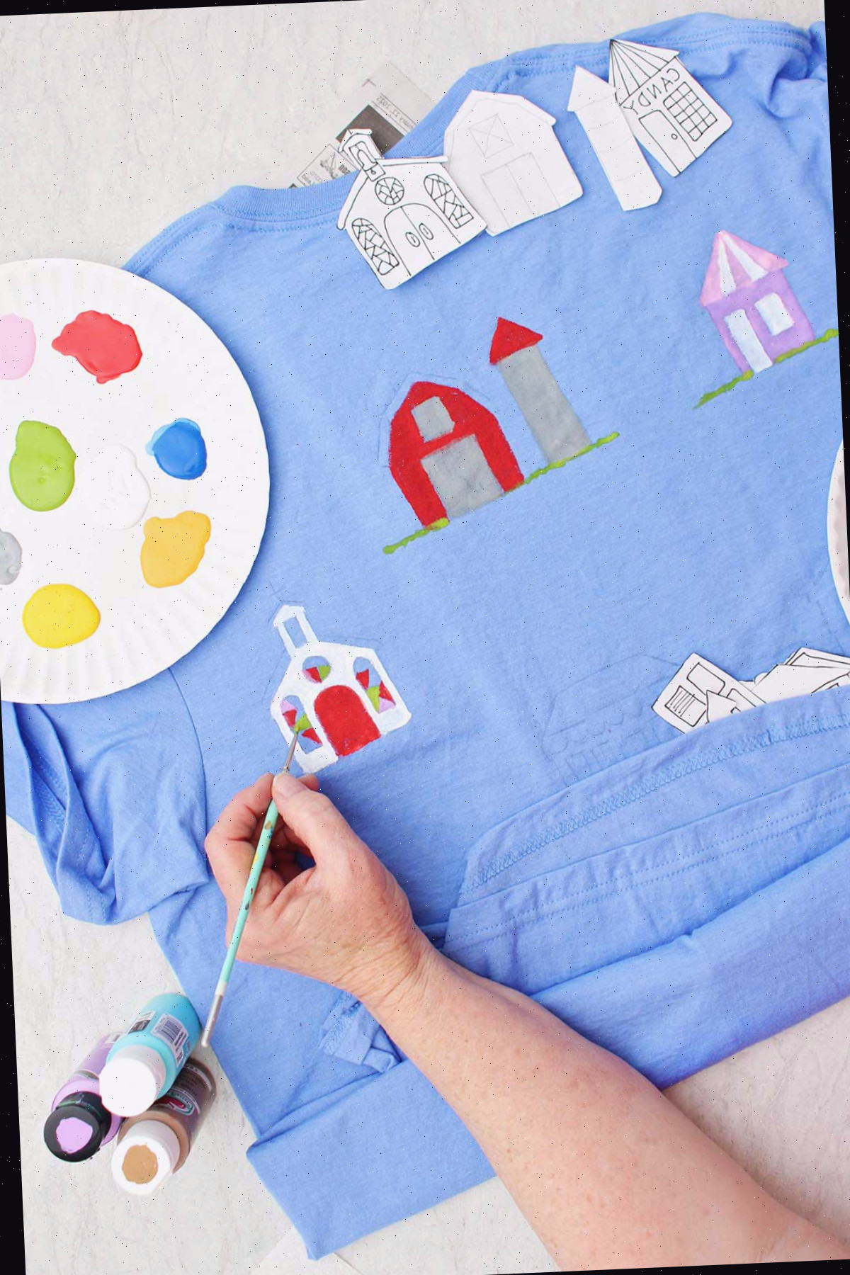 Uma pessoa pintando detalhes no vitral de uma igreja em uma camiseta azul com um prato de tinta por perto.