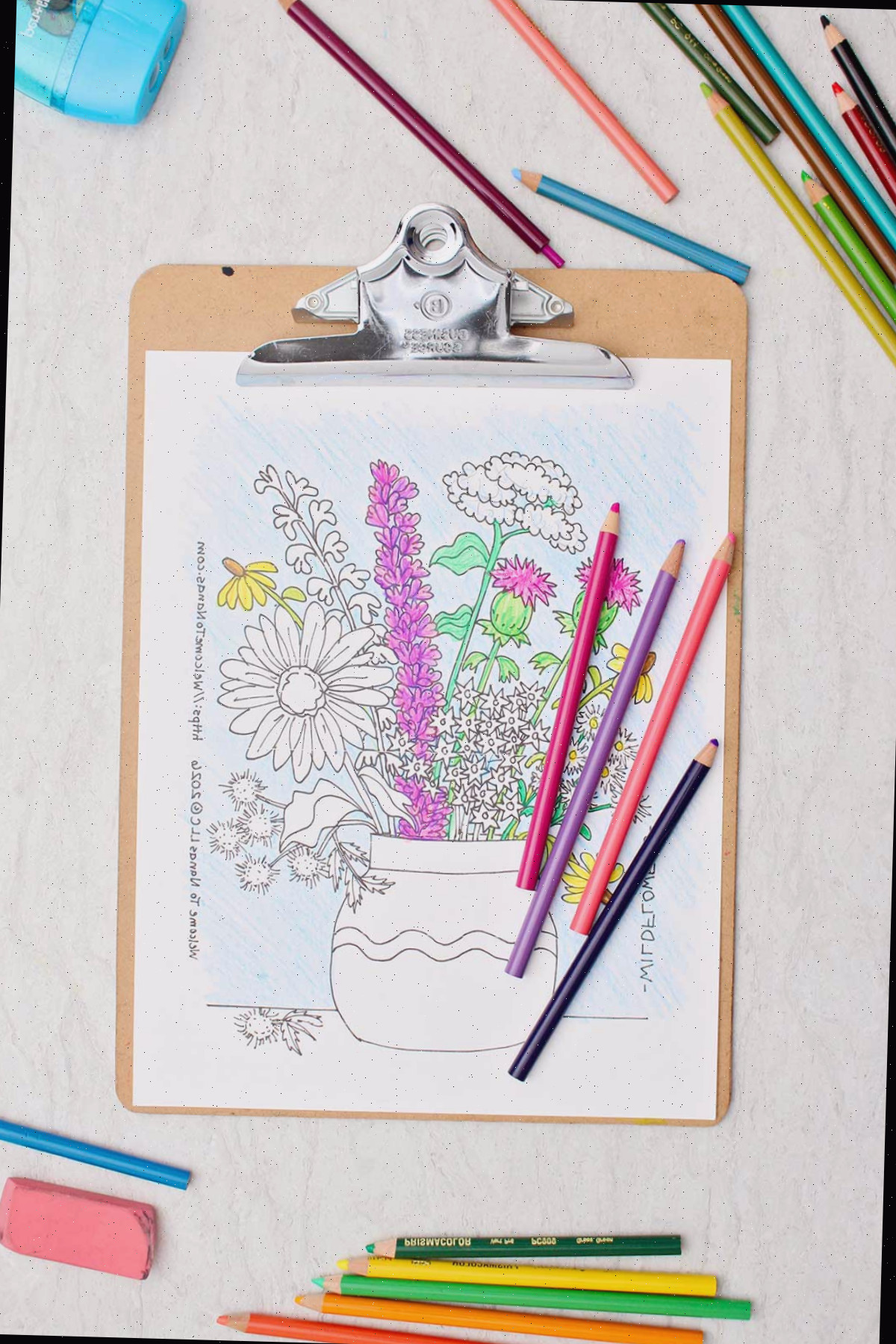 Uma página de colorir parcialmente finalizada de um buquê de flores silvestres em um vaso com lápis de cor ao redor.
