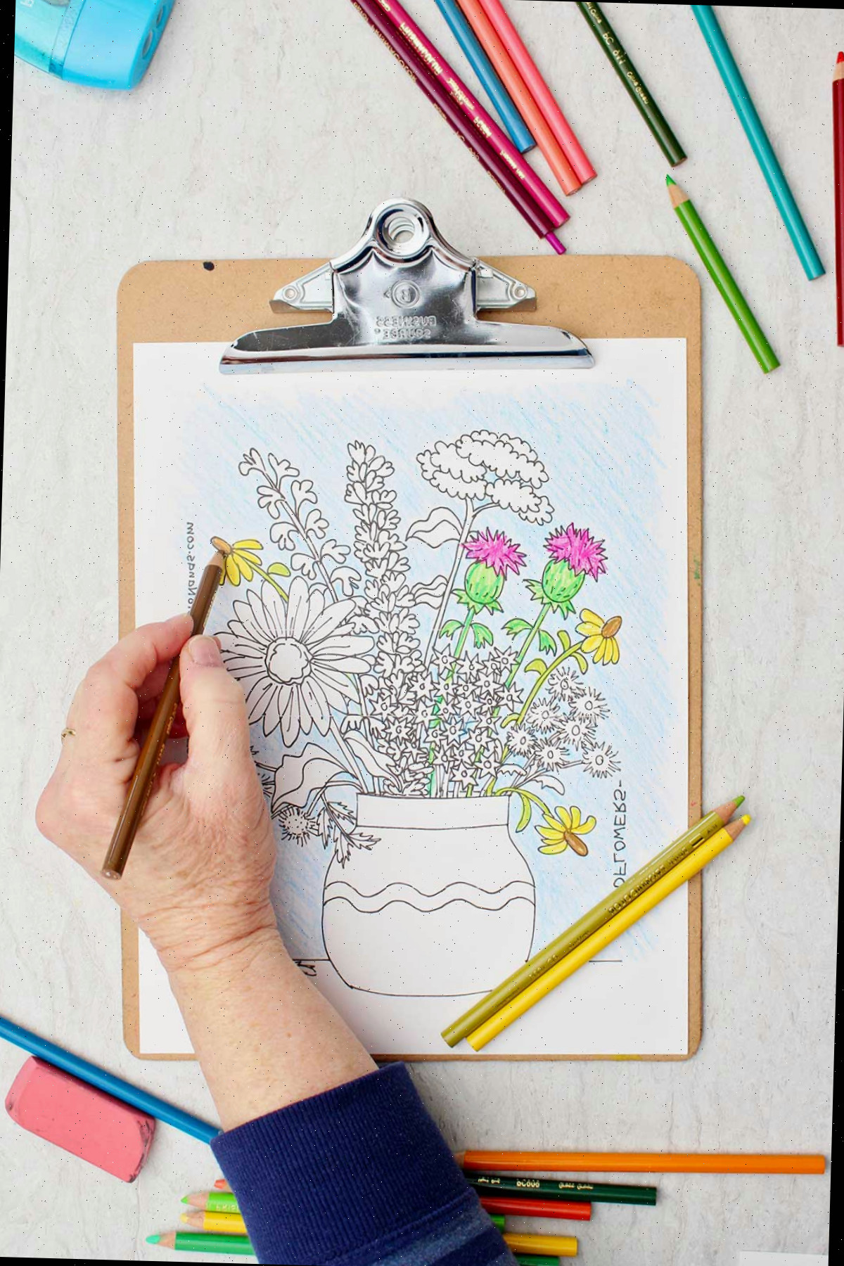 Pessoa colorindo uma margarida de amarelo na página de colorir de um buquê de flores silvestres em um vaso.