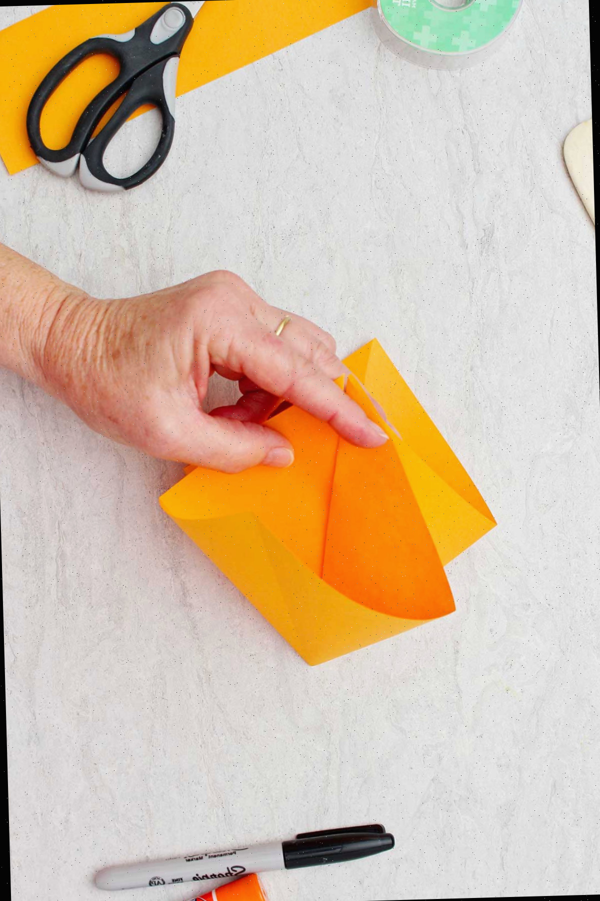 Pessoa mostrando a visão interna do papel laranja dobrado para fazer uma abóbora de origami.