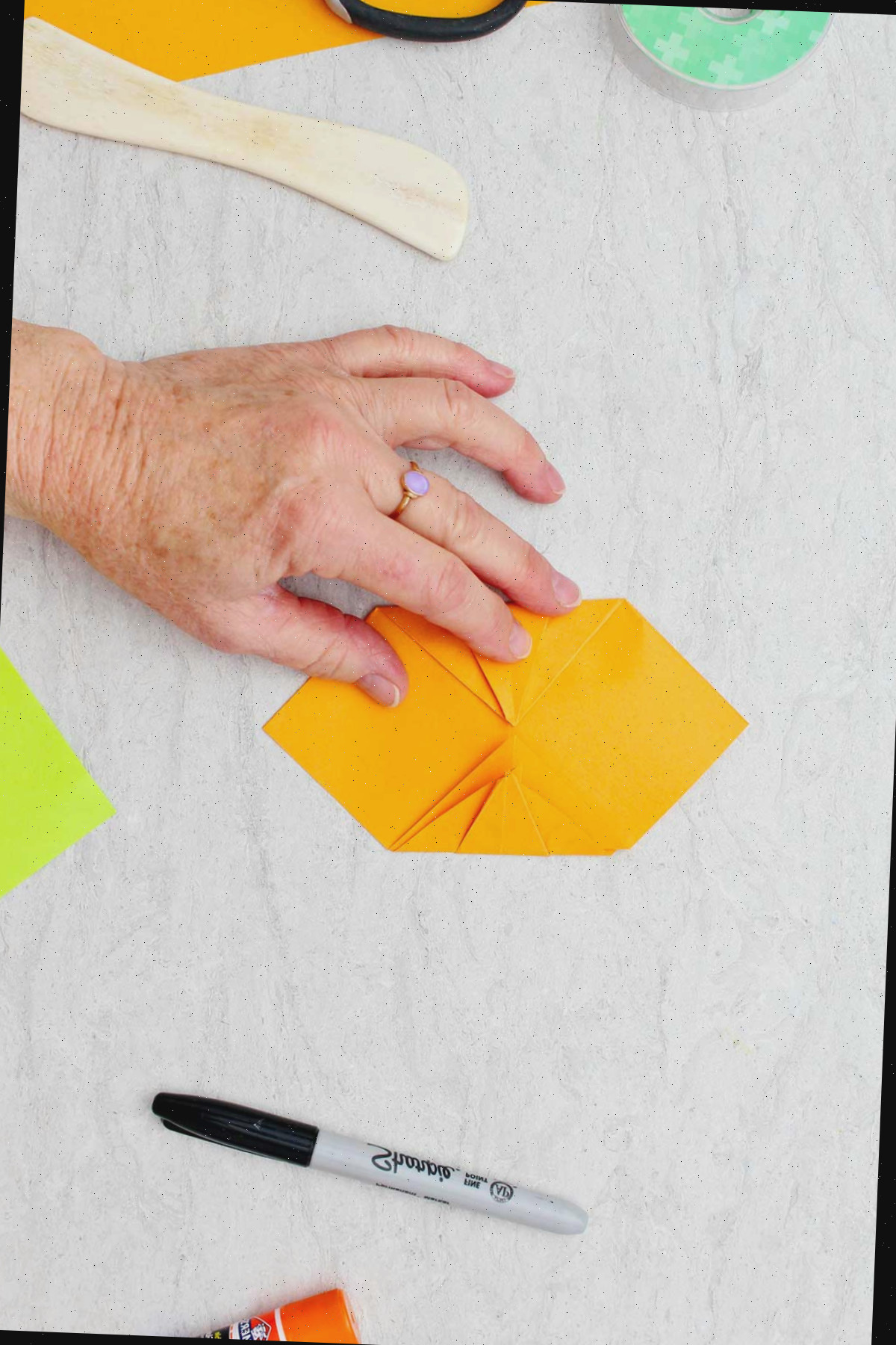 Indivíduo unindo duas laterais dobradas uma em direção à outra para criar uma abóbora de origami.