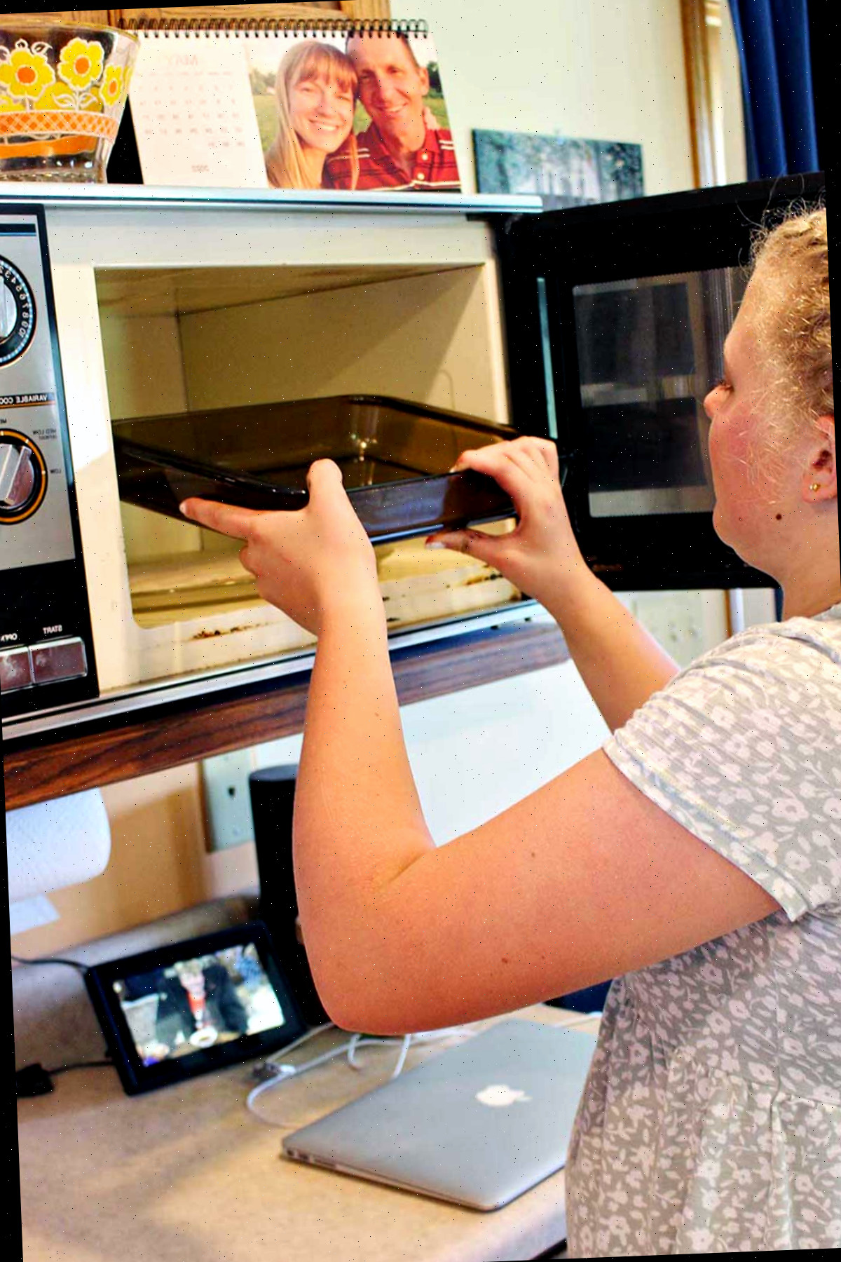 Uma jovem colocando um recipiente de vidro no micro-ondas.