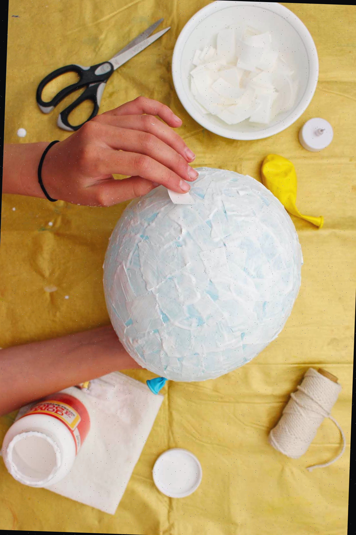 Indivíduo colocando pedaços de papel machê em um balão azul.
