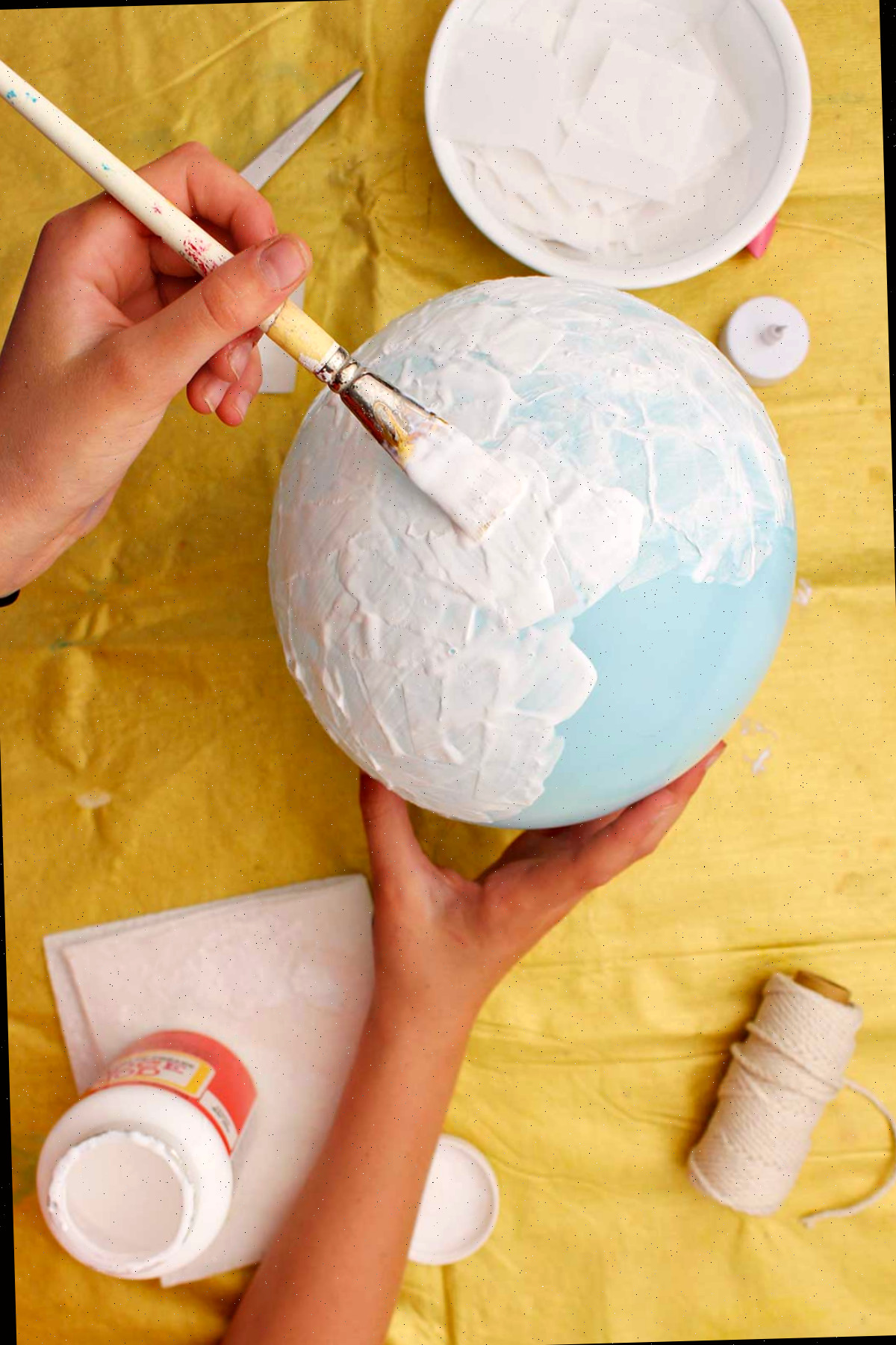 Indivíduo pintando um balão azul com mod podge.