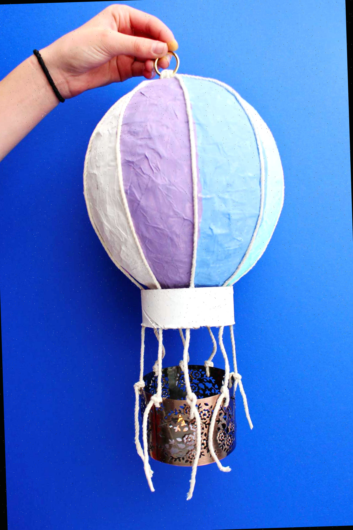 Indivíduo segurando um artesanato de mini balão de ar quente completado contra um fundo azul.