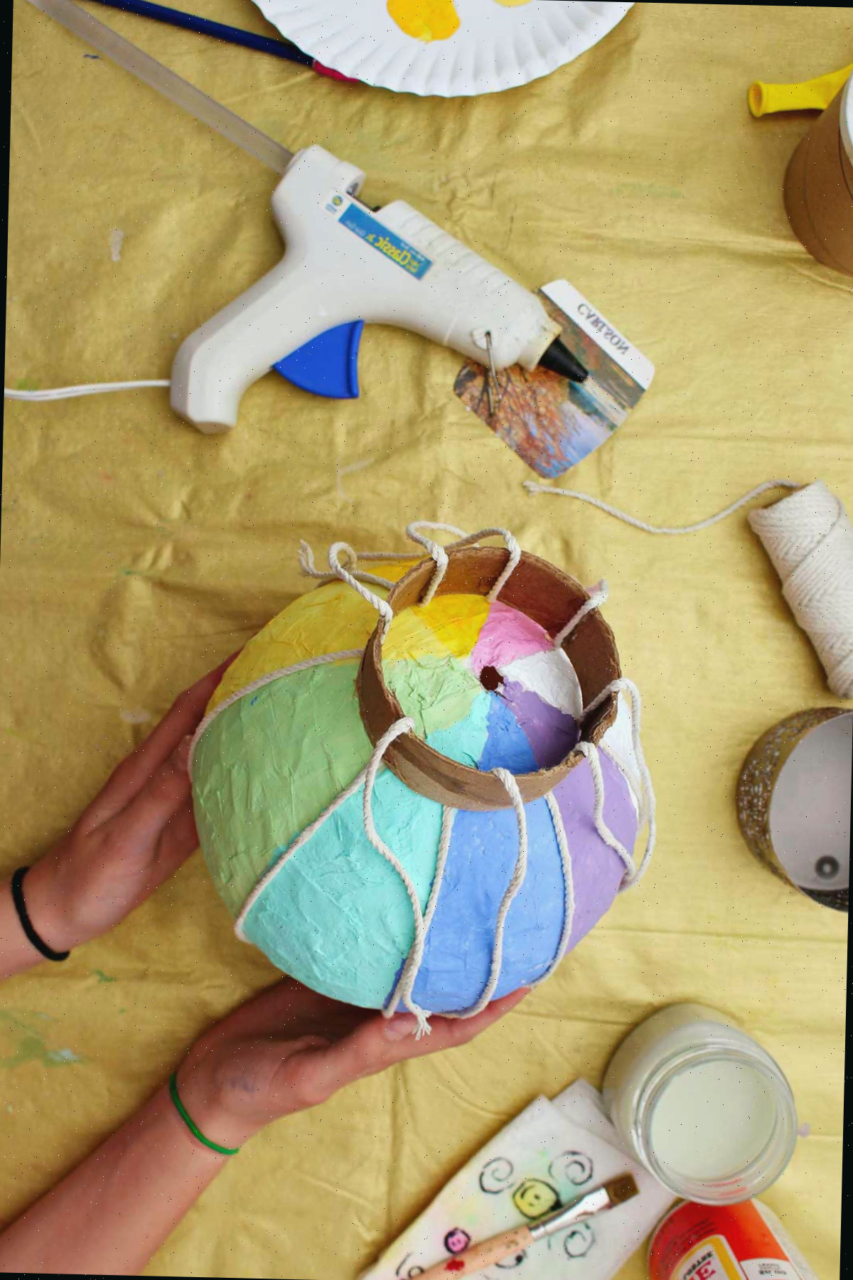 Indivíduo mostrando a parte inferior de um mini balão de ar quente com cordas preparadas para serem ligadas a uma cesta de metal.