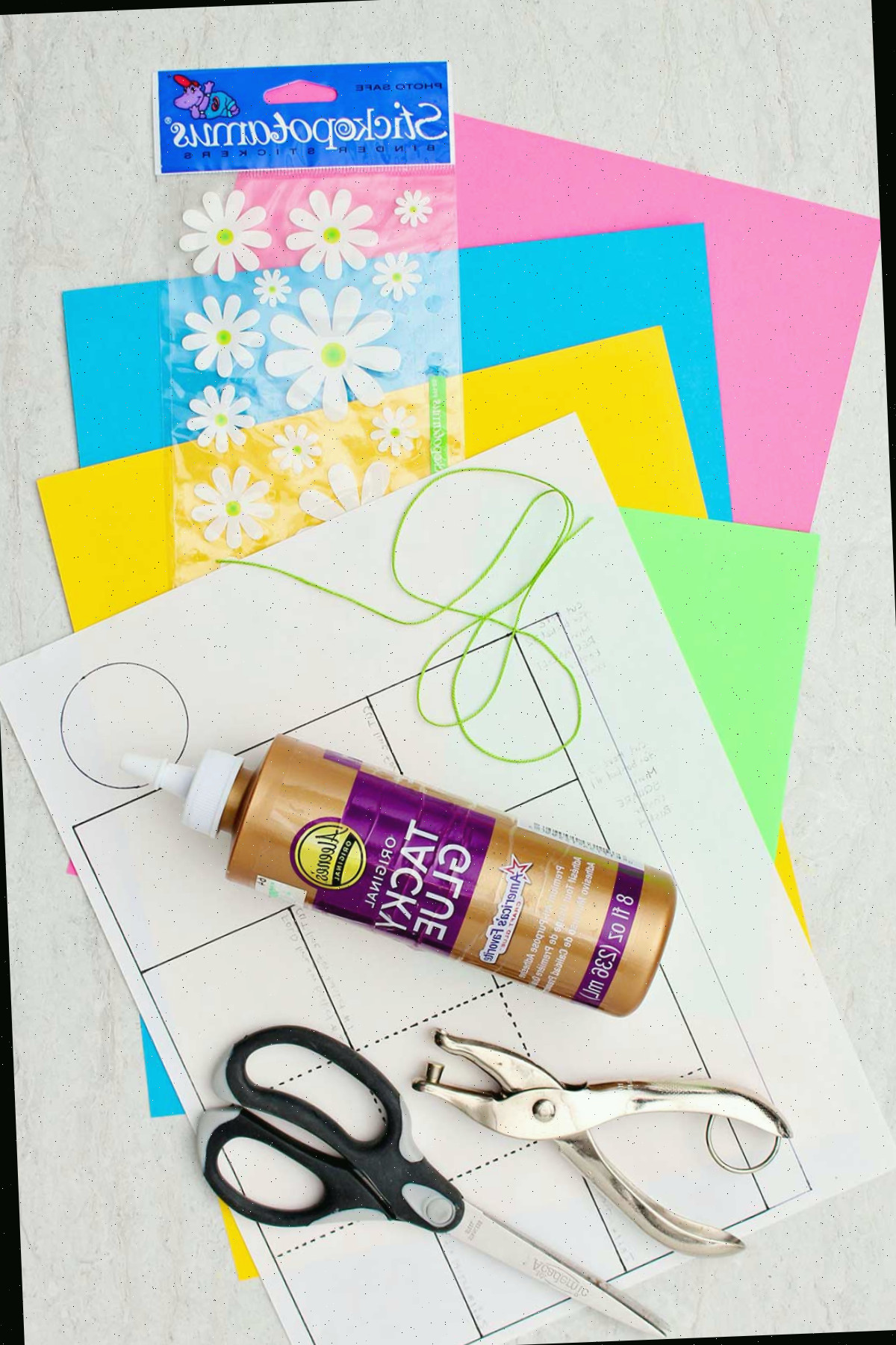 Um molde de mini cesto de Páscoa de papel, papel colorido, adesivos de flores, cola, tesoura e um perfurador.