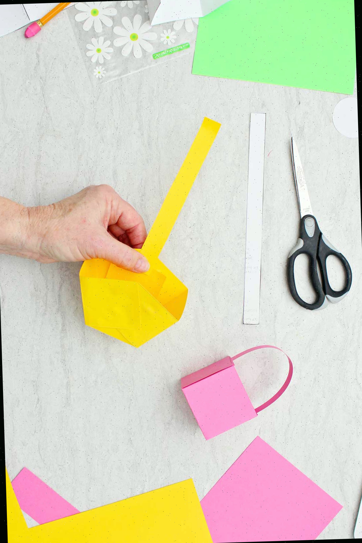Indivíduo fixando uma extremidade de um cabo por dentro de uma mini cesta de Páscoa amarela de papel com outros suprimentos nas proximidades.