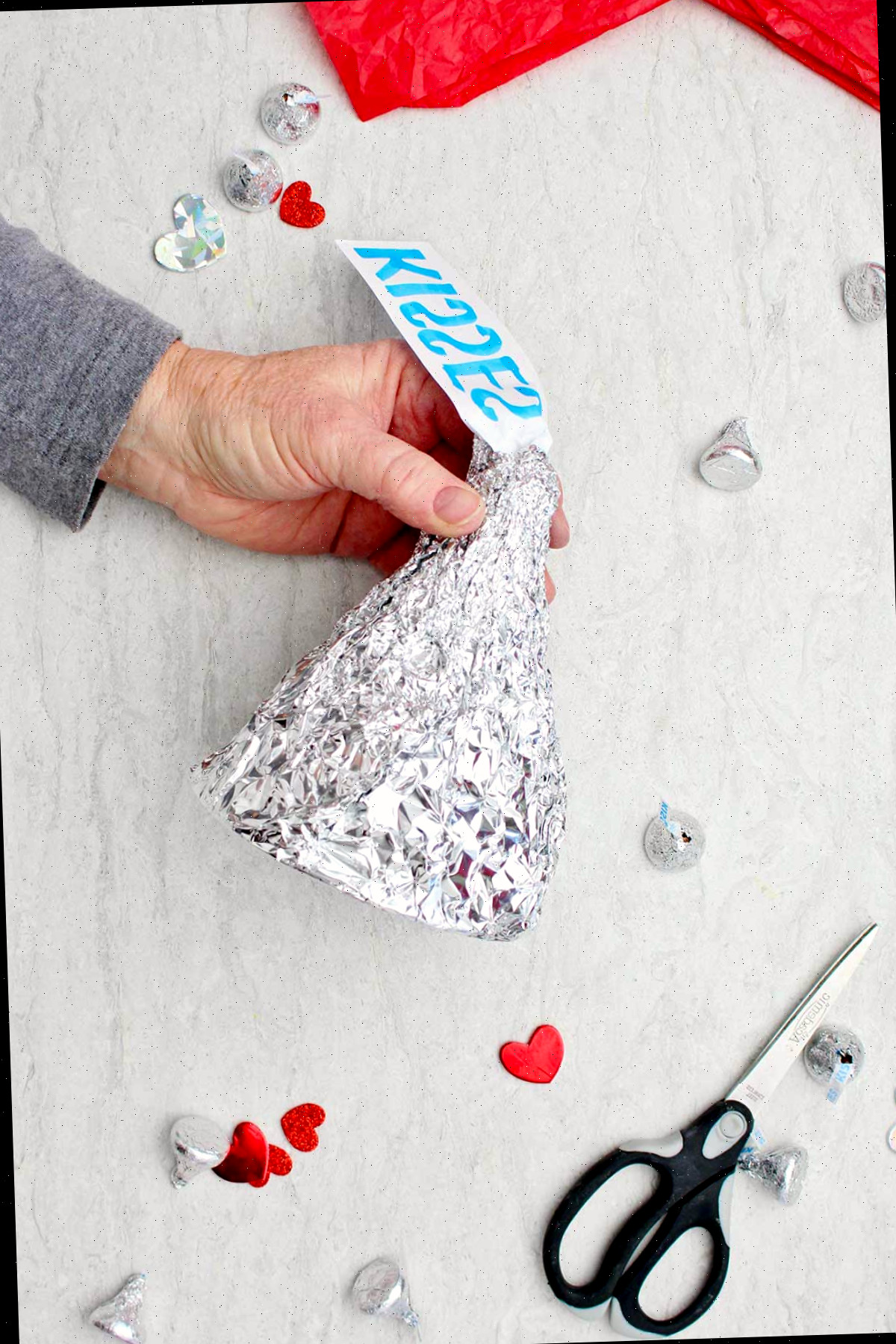 Pessoa segurando um Beijo Gigante de Hershey DIY finalizado com tesoura, decorações de coração e beijos espalhados ao redor.