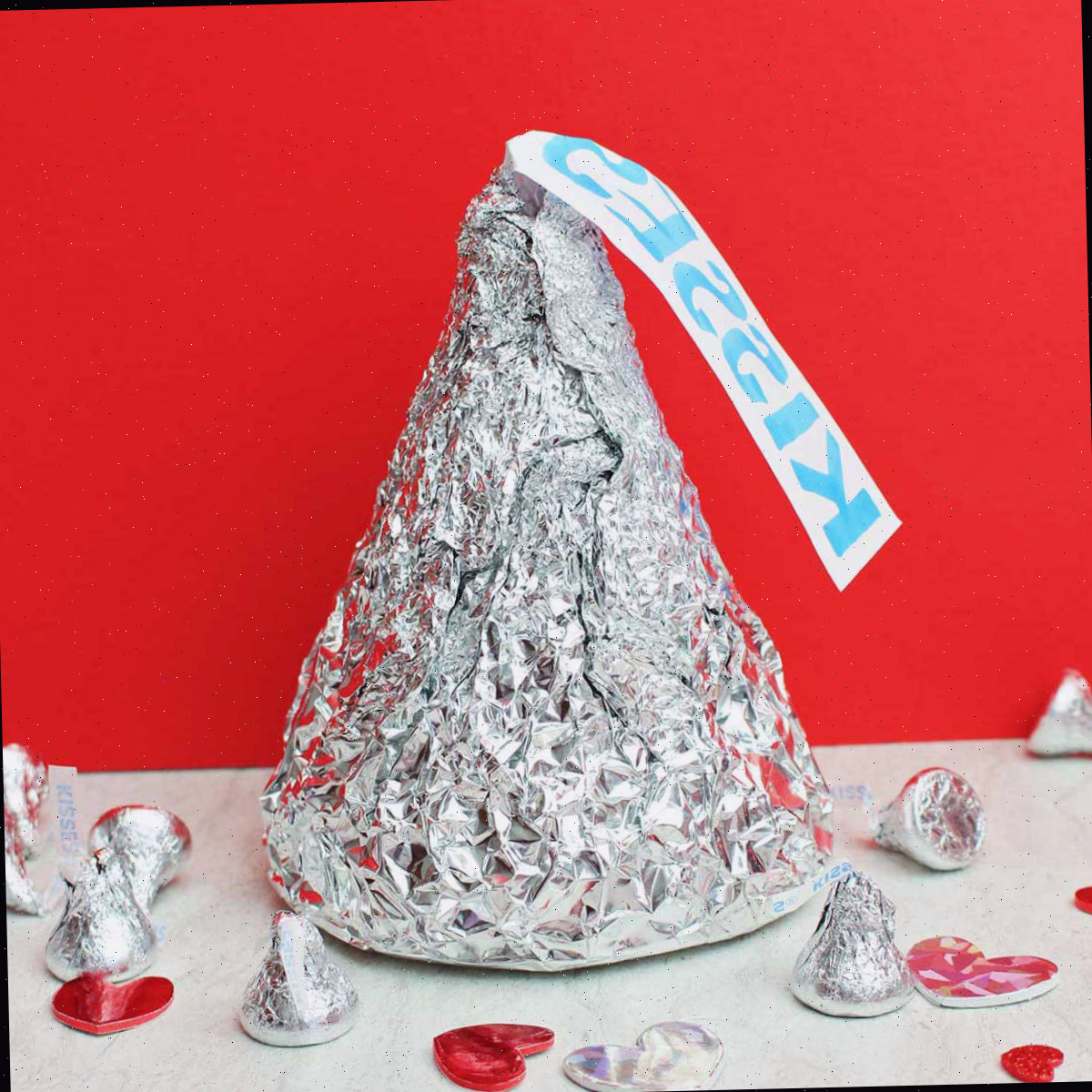 Giant Hershey Kiss com beijos em tamanho real e decorações de coração sobre um fundo vermelho.