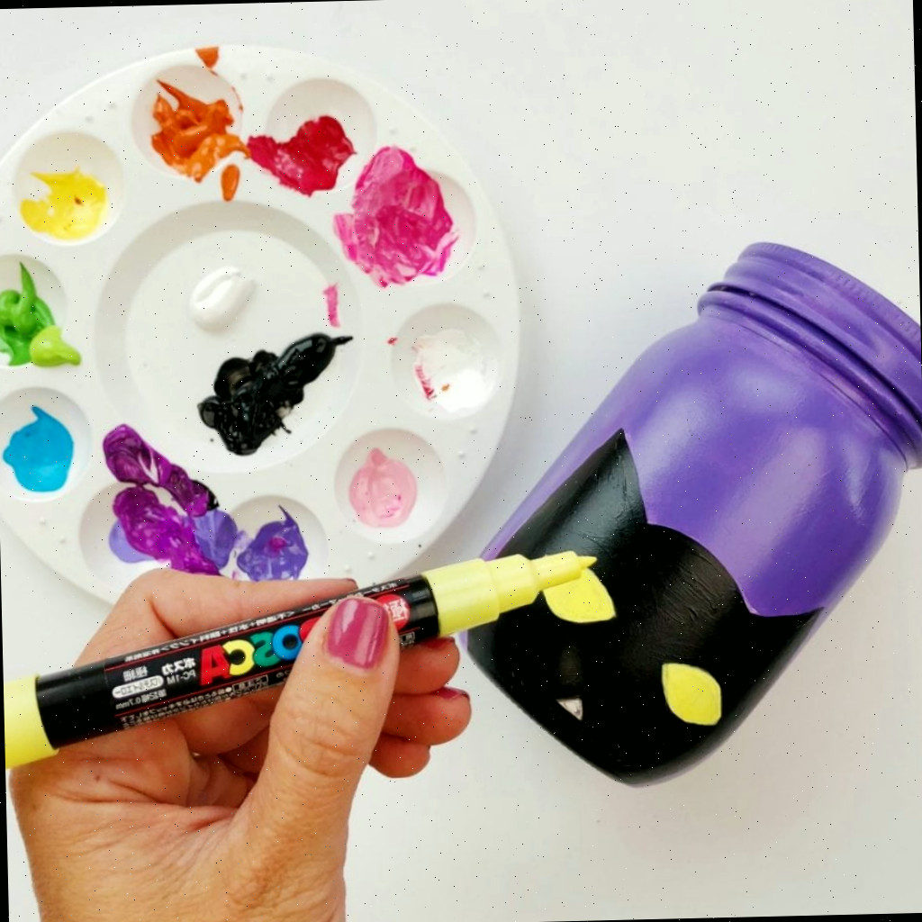 Frasco roxo com contorno de gato preto e olhos sendo adicionados em amarelo com uma caneta de tinta