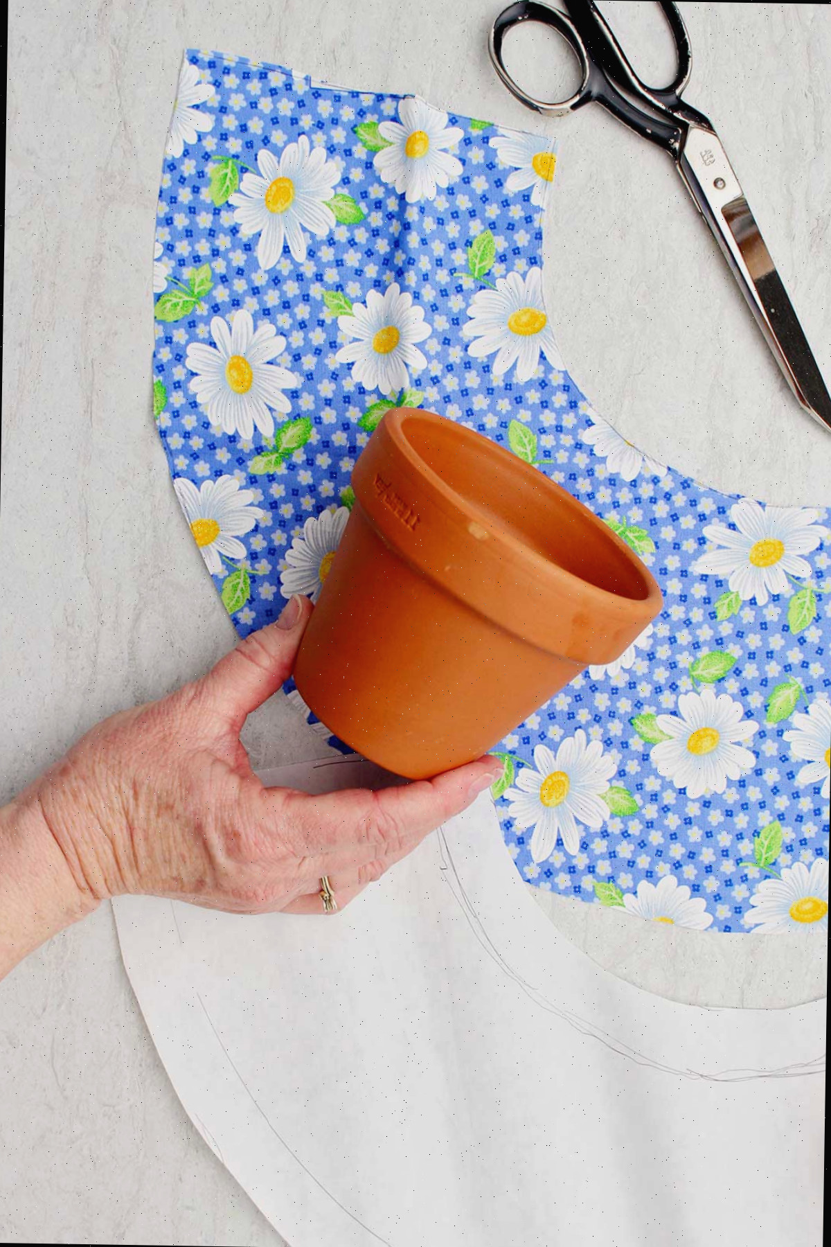 Uma pessoa segurando um pequeno vaso de flores com pedaços de tecido cortados ao redor.