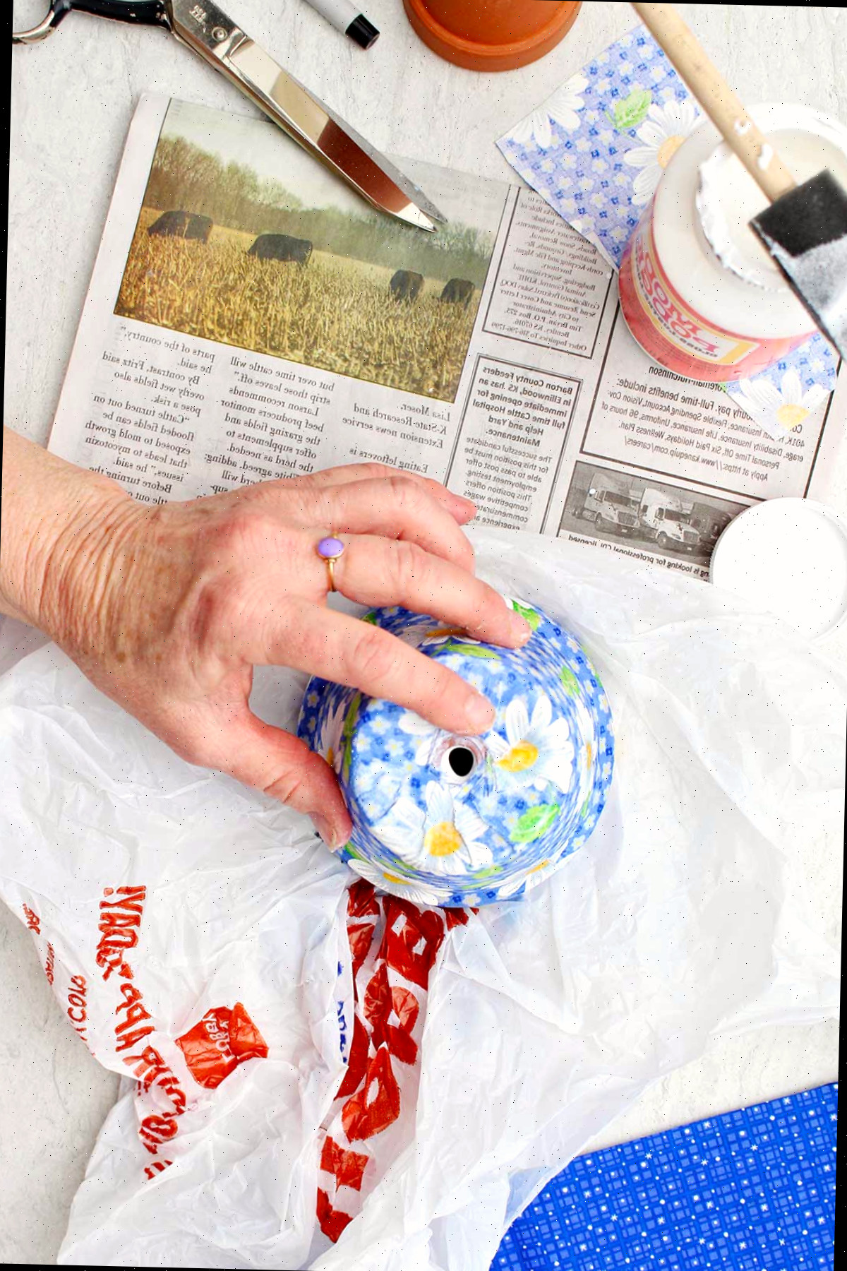Uma pessoa alisando o tecido azul de margarida em um vaso de flores com outros materiais por perto.