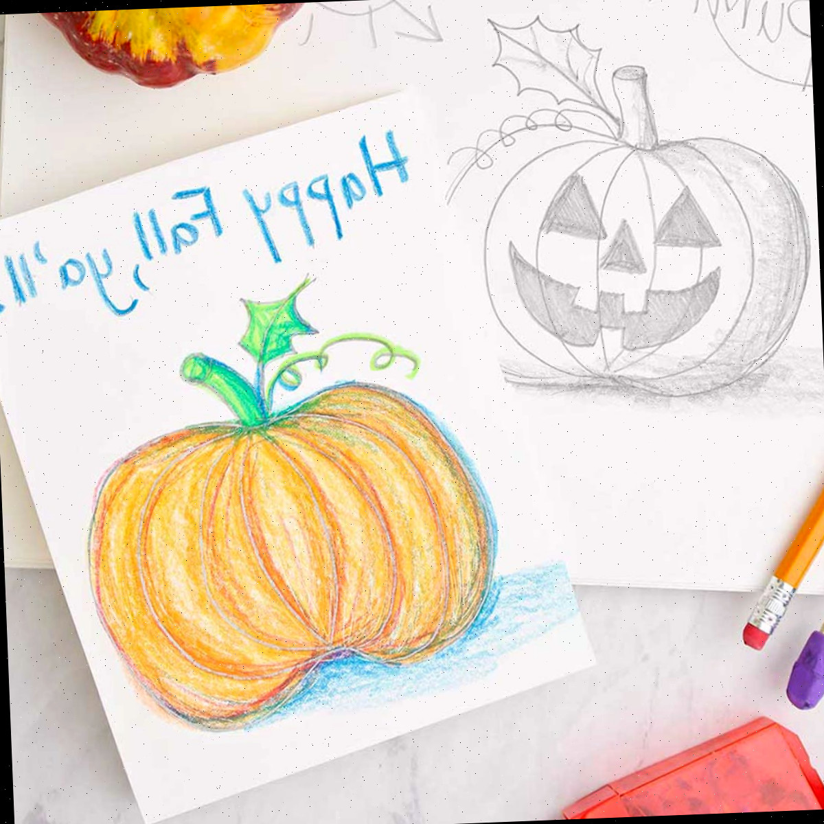 Um cartão de saudação com um esboço de abóbora colorida repousando sobre um esboço de lápis de jack-o-lantern. Materiais de desenho e coloração nas proximidades.