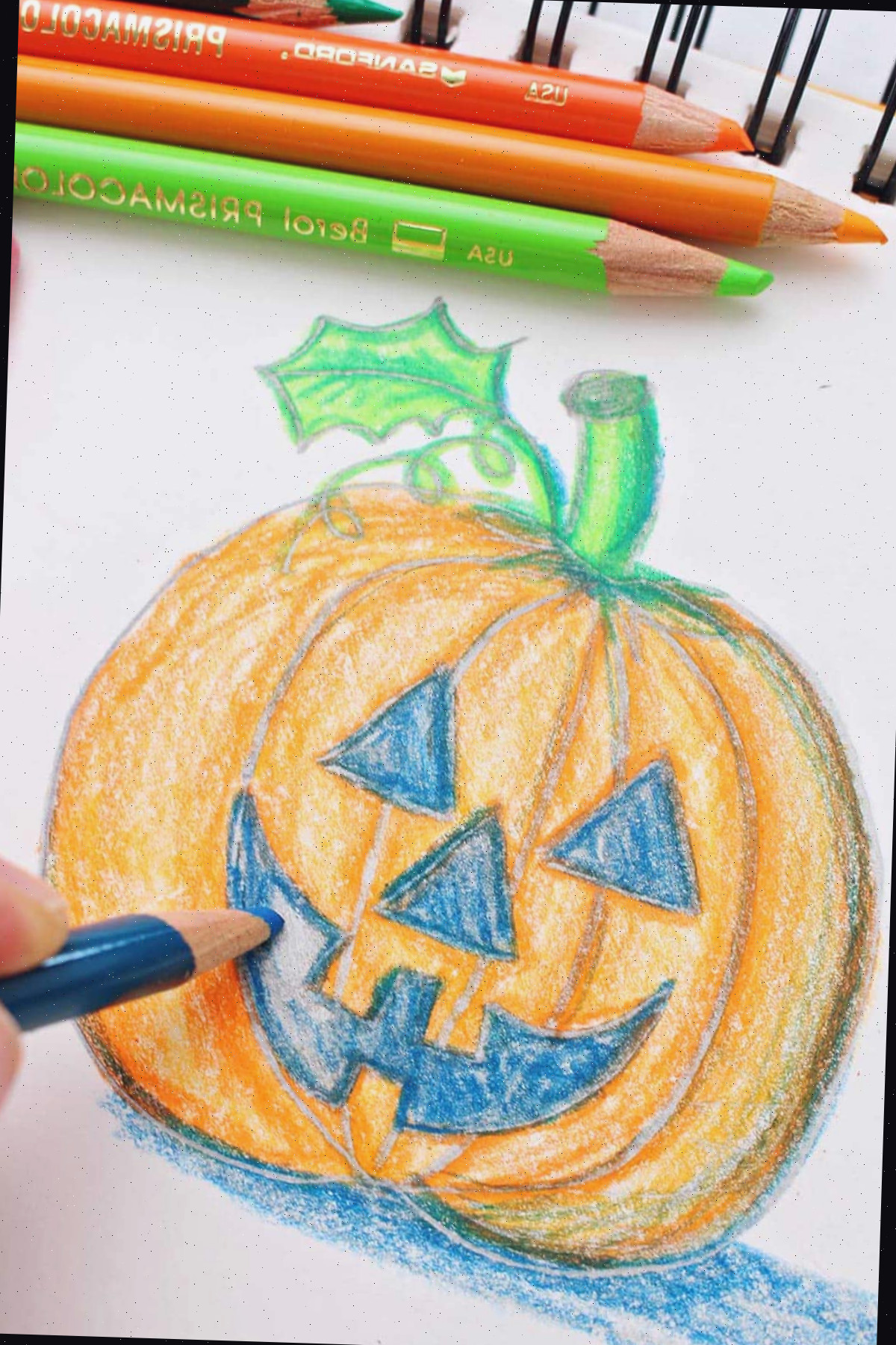 Mão colorindo a boca de um desenho de jack-o-lantern com lápis de cor.