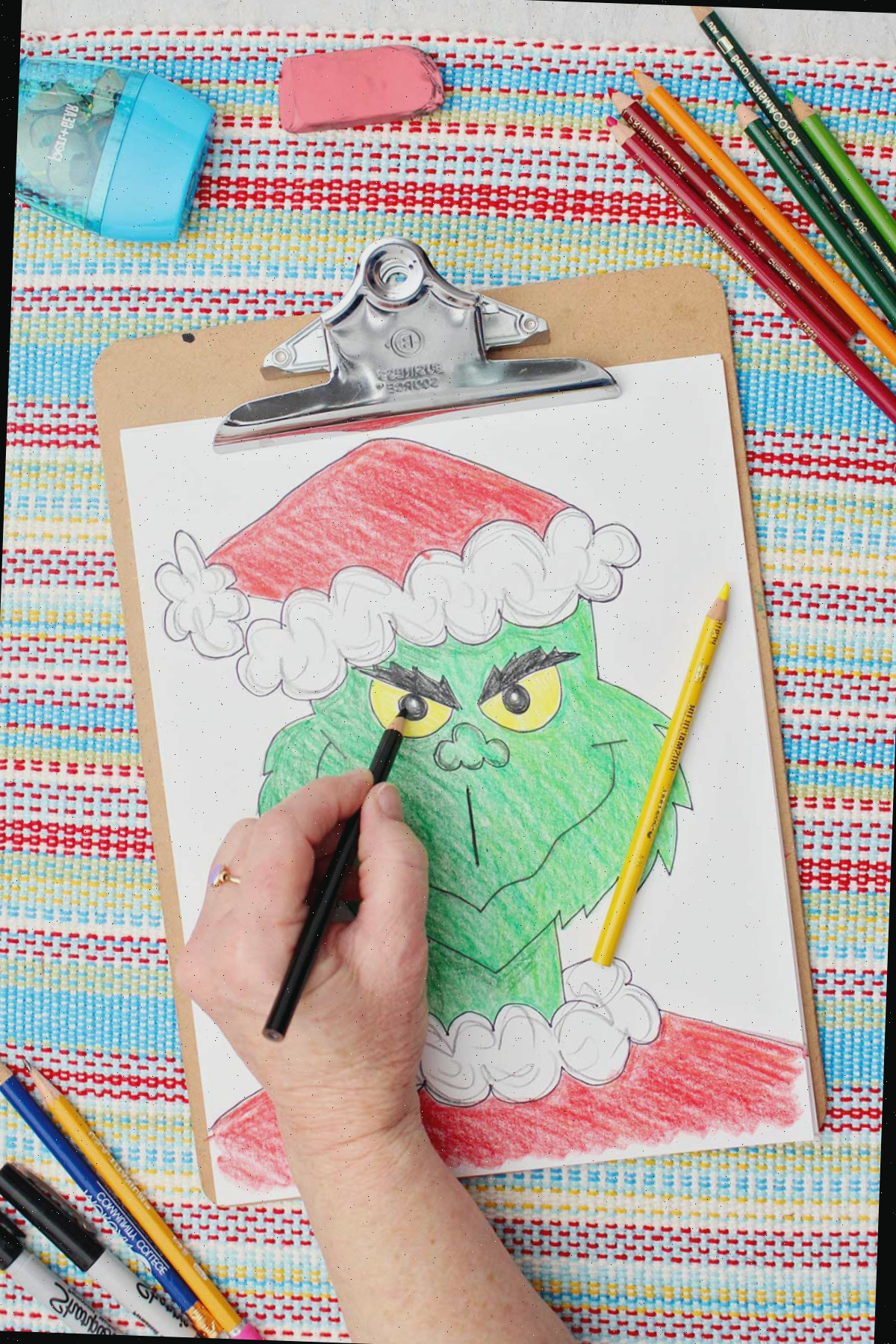 Pessoa colorindo as pupilas do Grinch de preto em uma versão colorida de um esboço do Grinch.