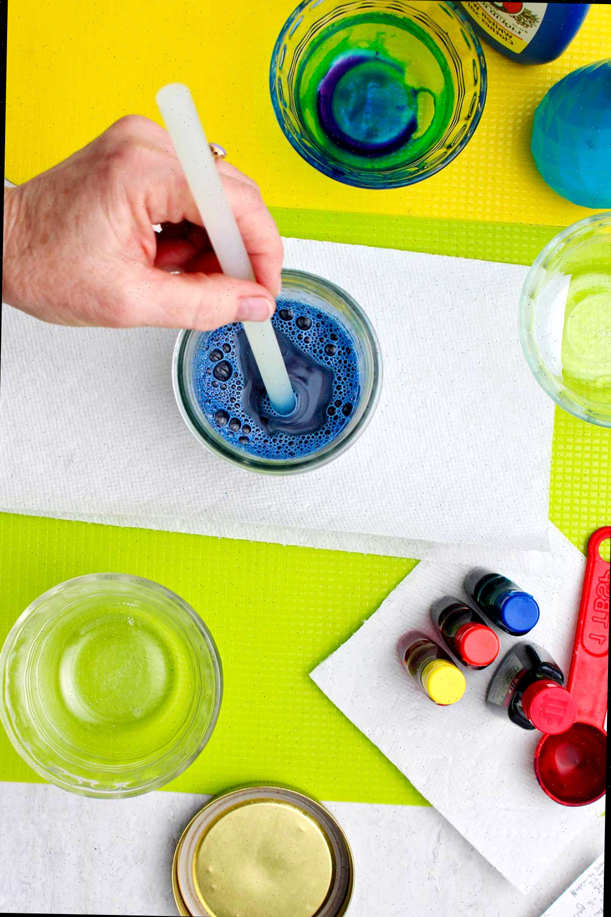 Mão segurando um canudo plástico em um copo com líquido de sabão azul.