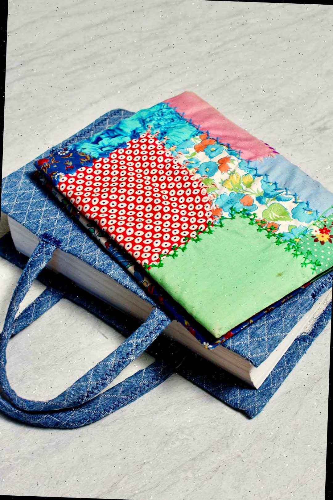 Duas capas de livro de tecido finalizadas. Uma com um padrão colorido de patchwork e outra com tecido de denim.