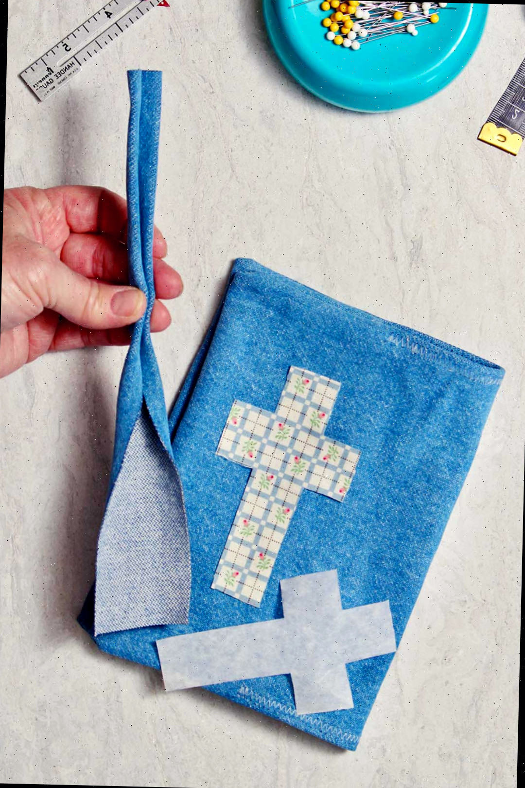 Uma mão segurando uma pequena tira de tecido de denim que será utilizada como alça para a capa de livro de denim.