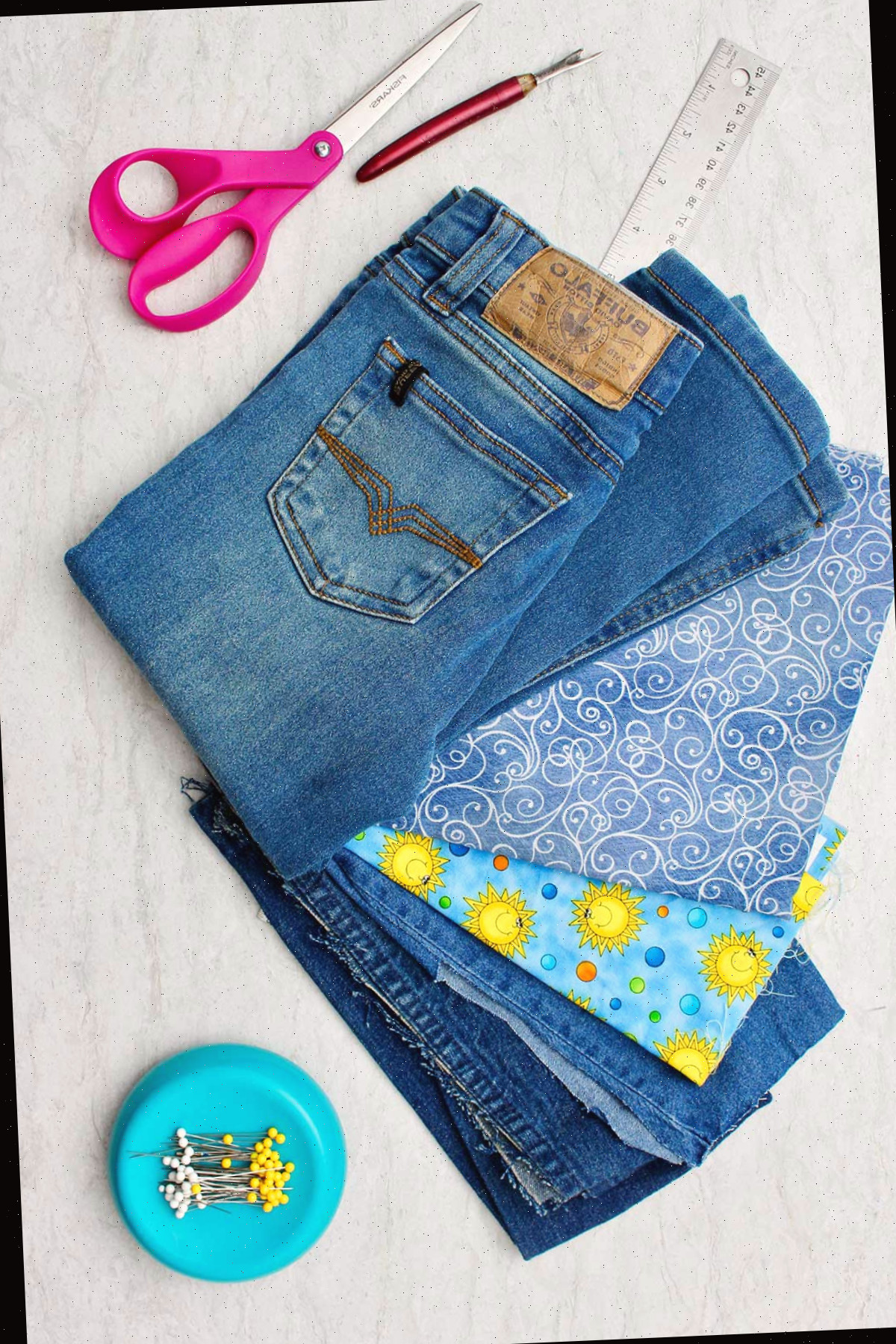 Materiais necessários para fazer jeans de barra de sino: um par de jeans, tesoura, tecido decorativo, régua e alfinetes.