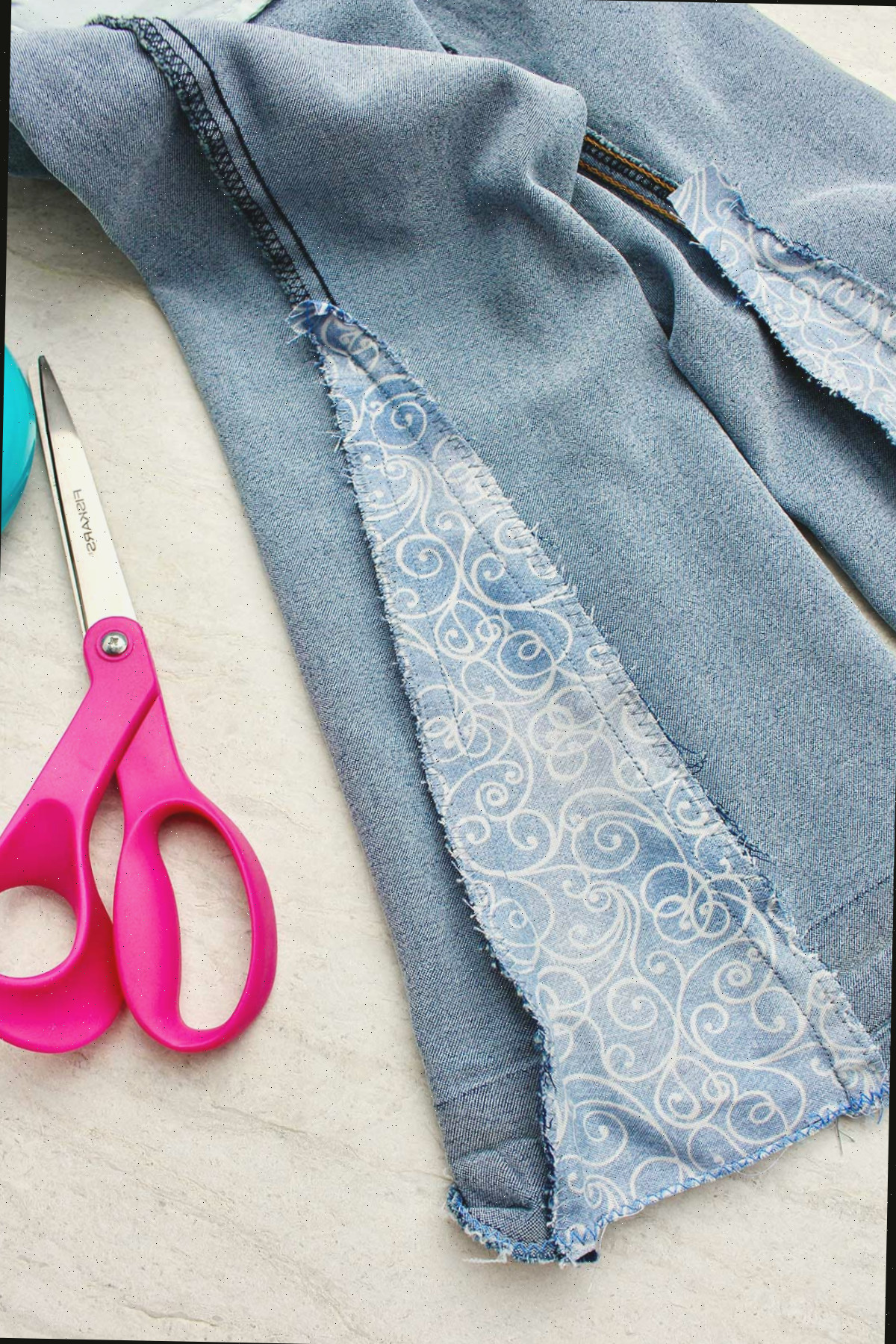 Close da parte de dentro de um jeans do avesso com um pedaço de tecido costurado junto, com tesouras por perto.