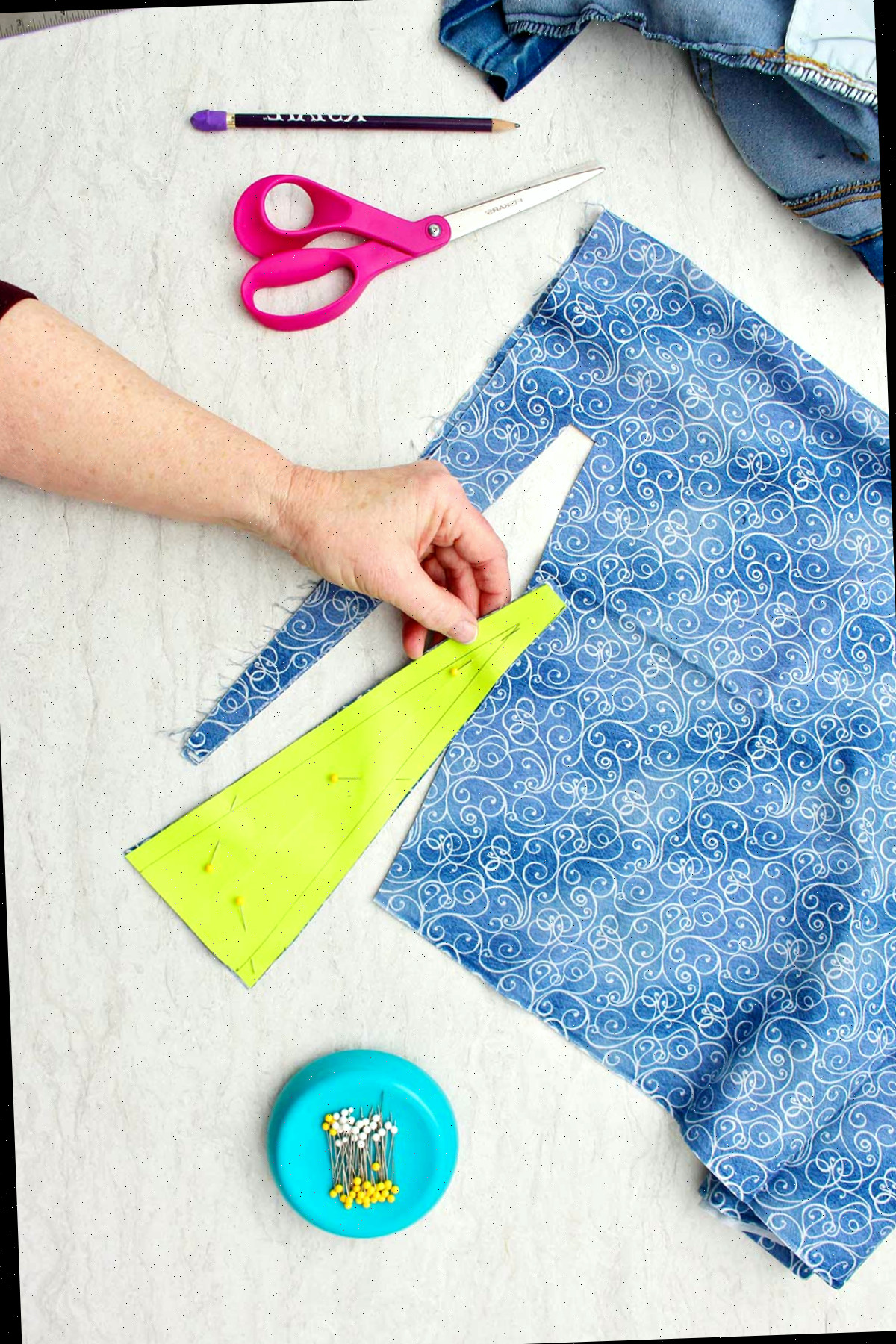 Mão segurando um recorte de tecido decorativo preso ao molde de papel com alfinetes retos.