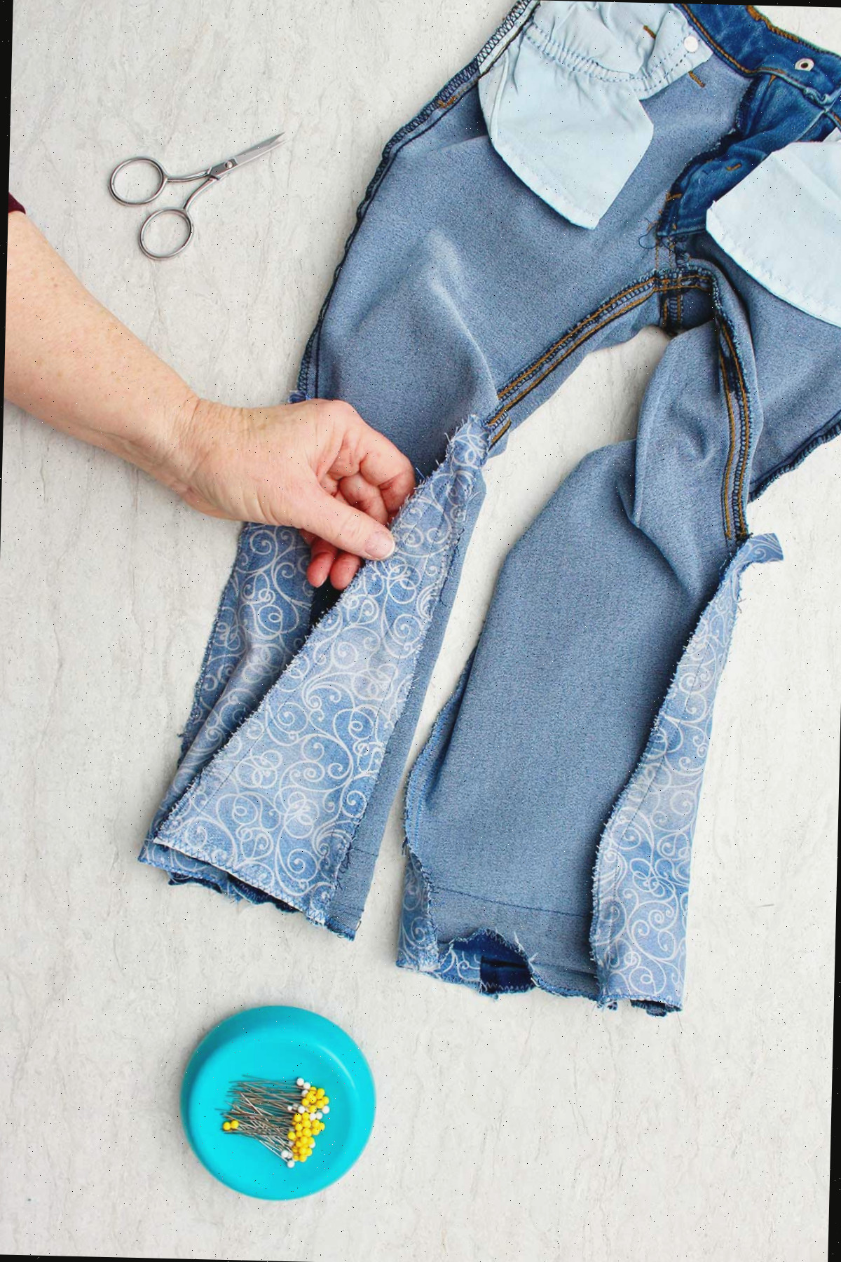 Mão mostrando jeans do avesso com um pedaço de tecido costurado para fazer barra sino.