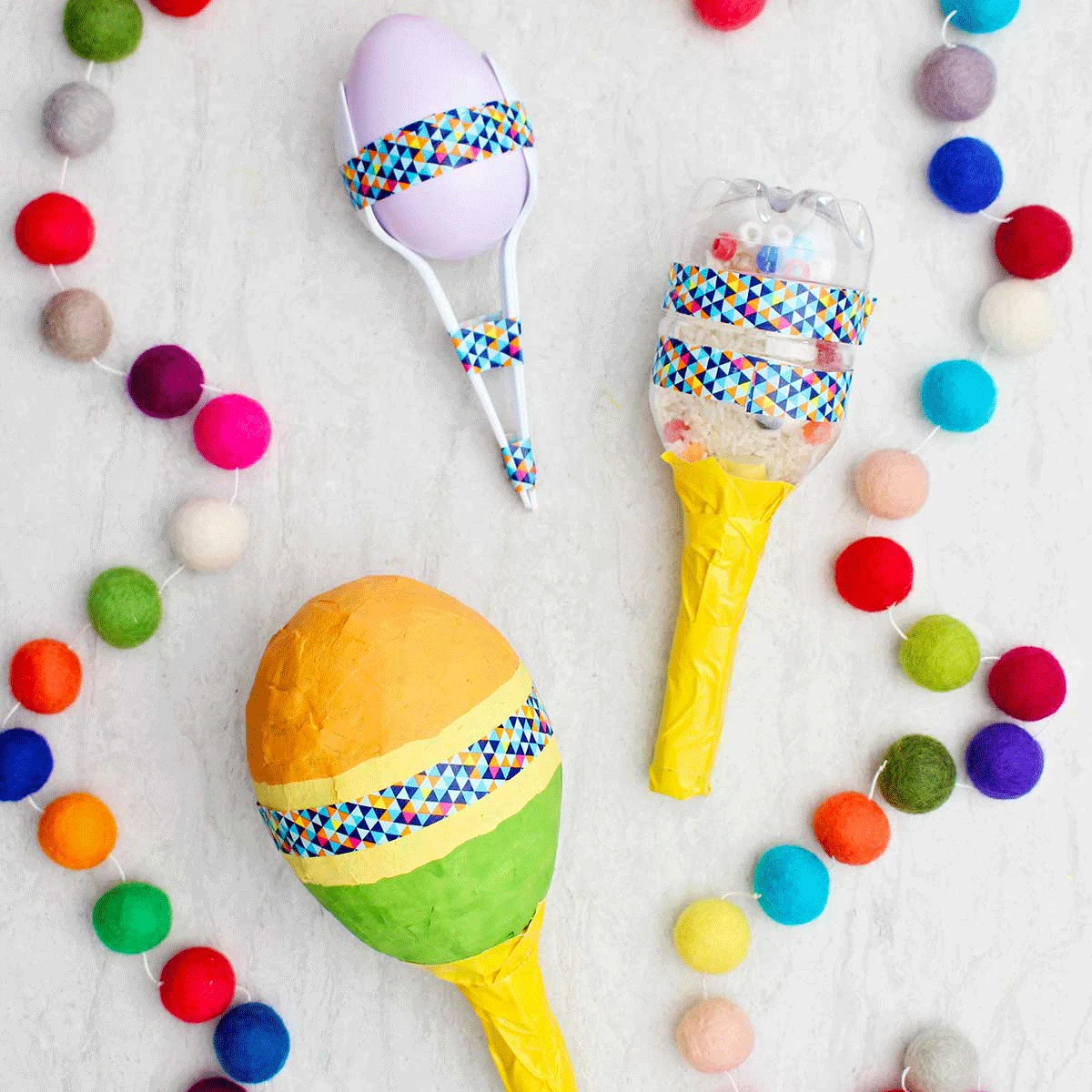 Três maracas diferentes completas com pom pons coloridos próximos.