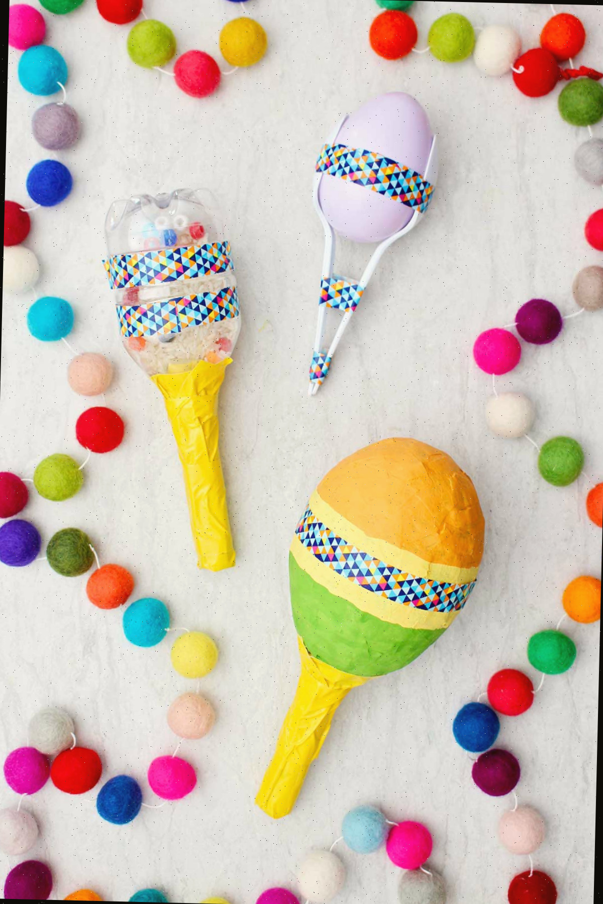 Três maracas completas diferentes com pompons coloridos ao lado.