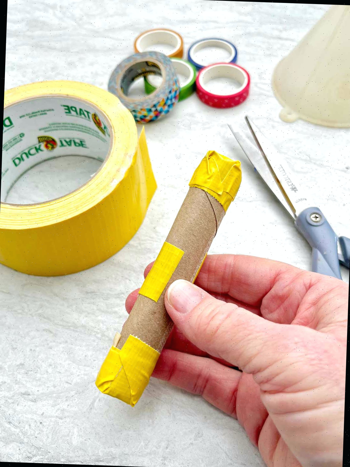 Pessoa demonstrando como segurar um rolo de papel toalha junto para criar um cabo de maraca.