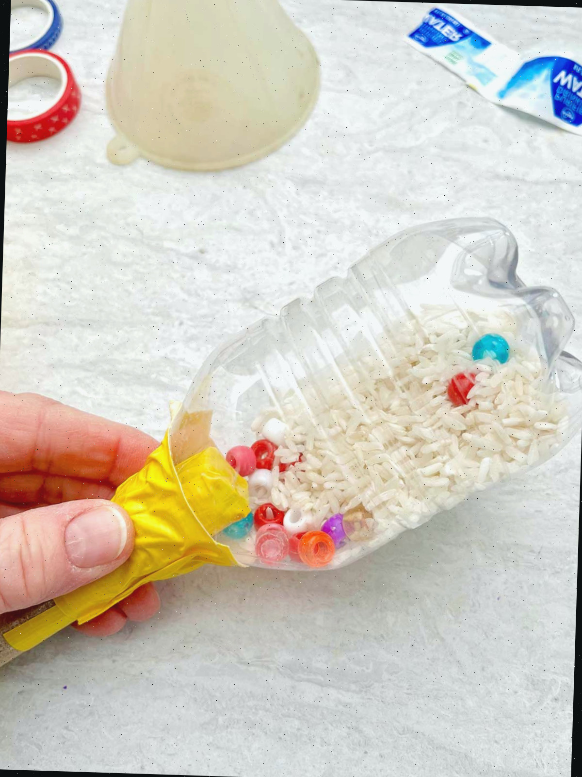Pessoa segurando a maraca de garrafa com água para mostrar o arroz seco e as miçangas no interior.