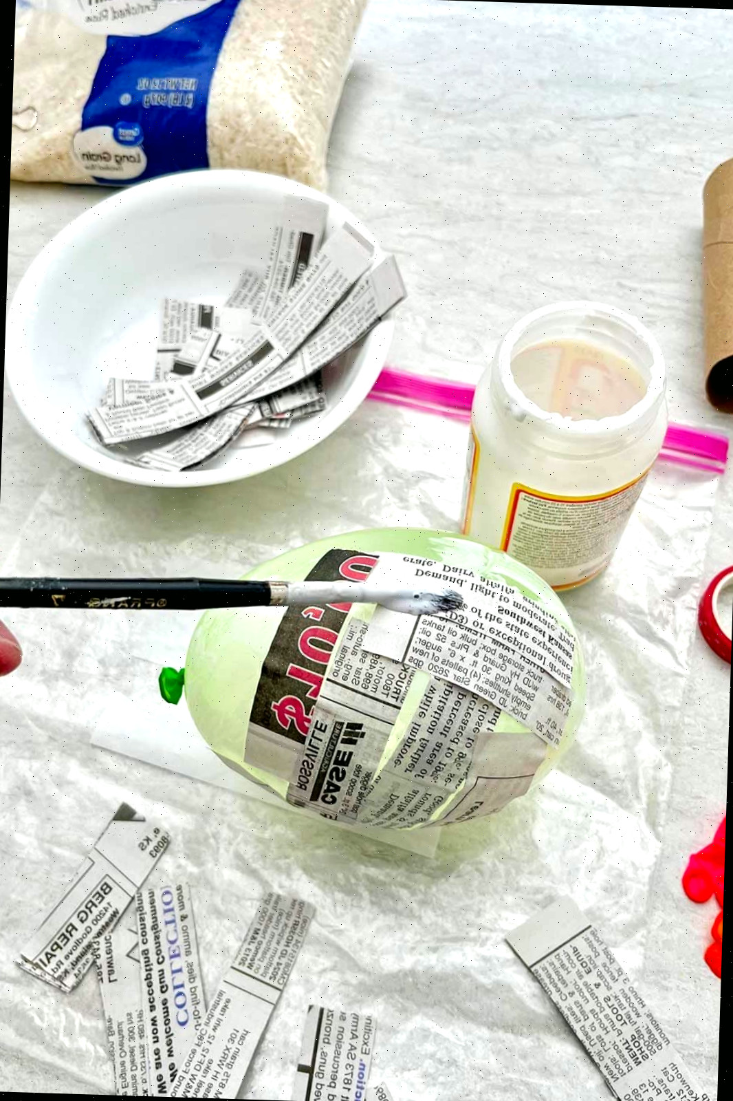 Pessoa pintando tiras de papel de jornal em um balão com mod podge.