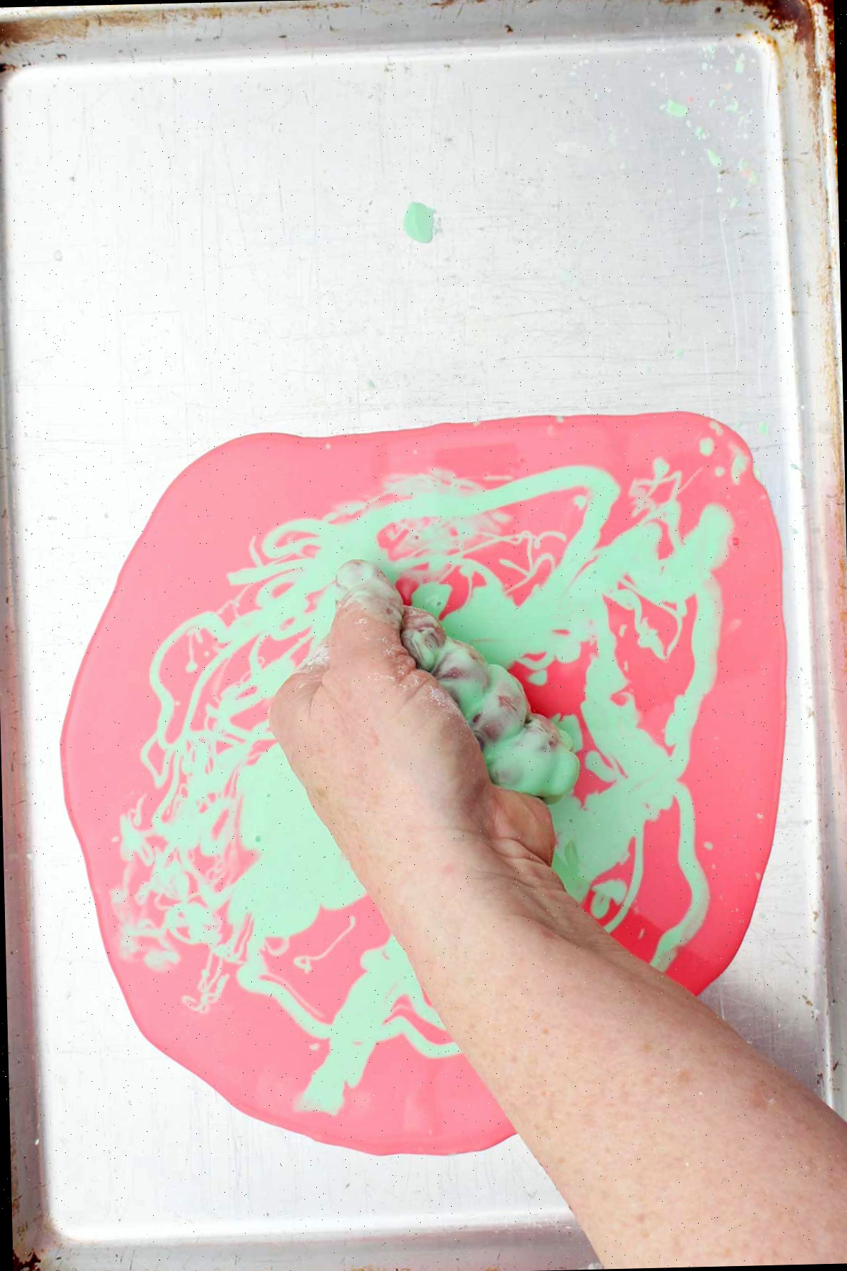 Uma pessoa apertando um punhado de oobleck sobre uma assadeira.