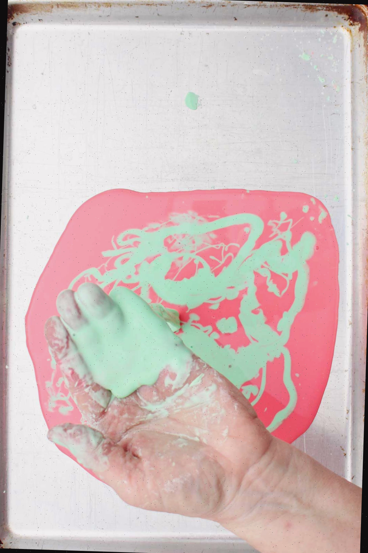Uma pessoa segurando um punhado de oobleck verde claro sobre uma assadeira.