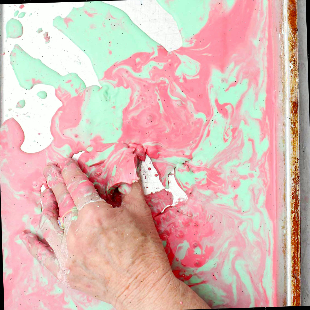 Uma pessoa pegando um pedaço semissólido de oobleck rosa e verde de uma assadeira.