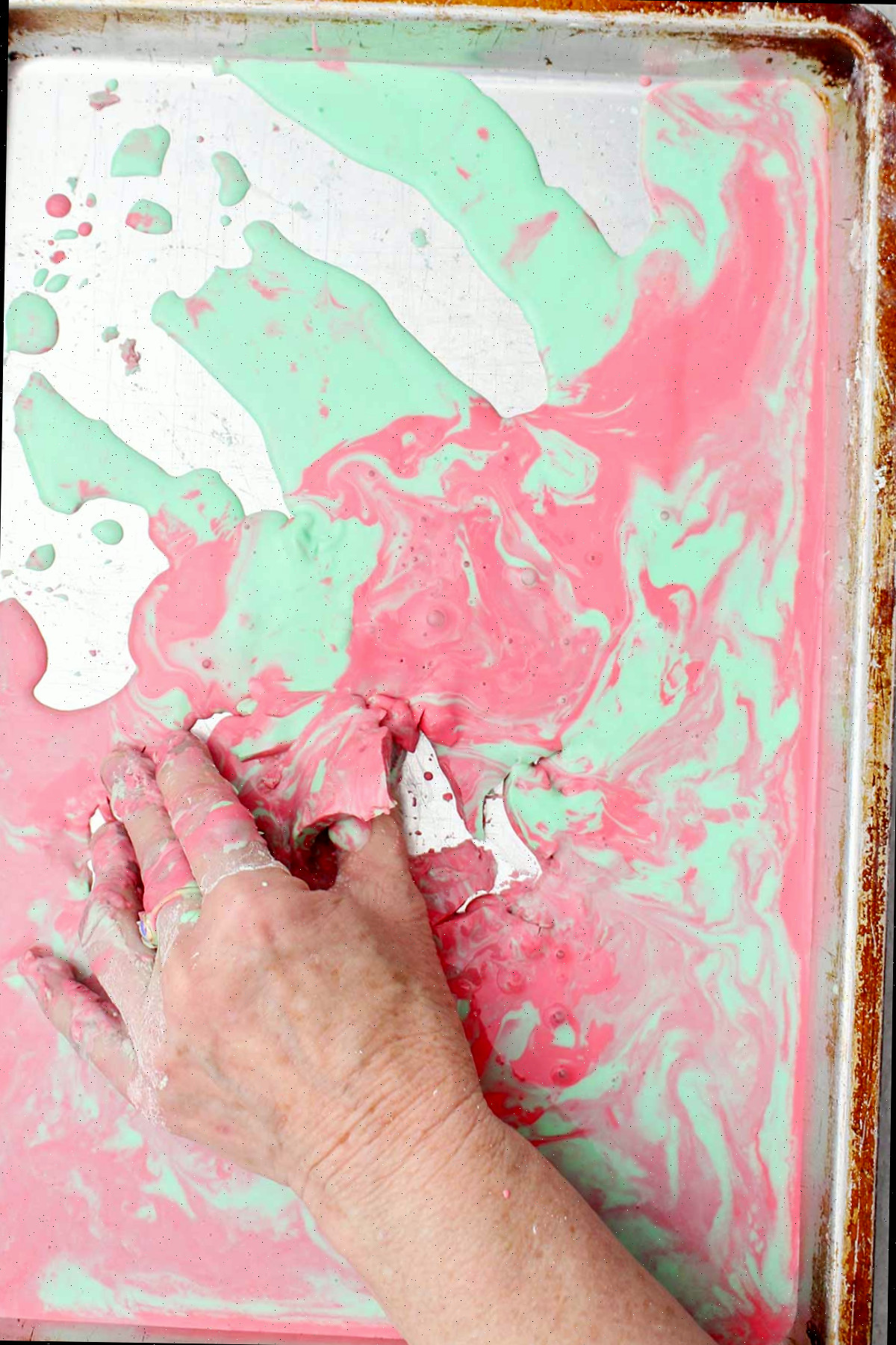 Uma pessoa pegando um pedaço semi sólido de oobleck rosa e verde de uma assadeira.