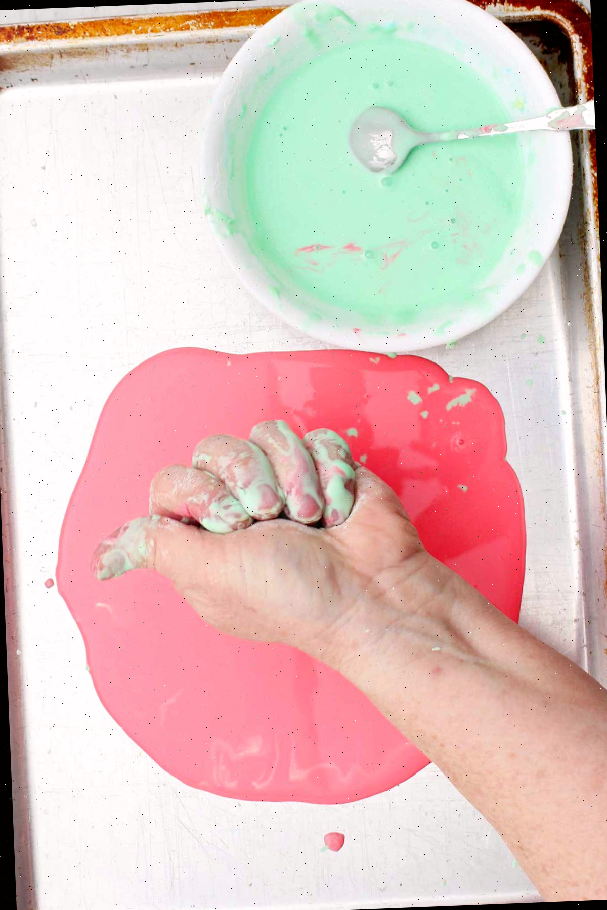 Uma pessoa apertando um punhado de oobleck sobre uma assadeira.